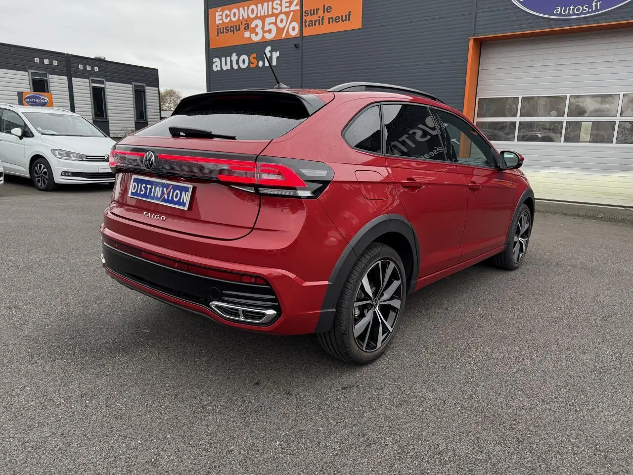 Vue 3/4 arrière droite d'un Volkswagen Taigo Rouge Roi avec jantes noires brillantes et feux arrière LED allongés.