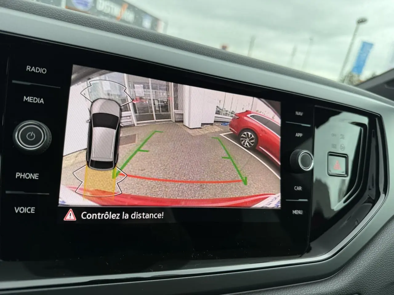 Vue de l'écran tactile intérieur montrant la caméra de recul du Volkswagen Taigo Rouge Roi avec aide au stationnement active.