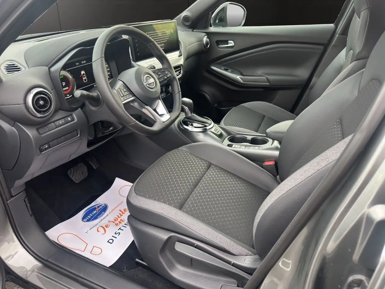 Vue intérieure côté conducteur du Nissan Juke 2025 gris squale, avec sièges et volant chauffants, tableau de bord digital et console centrale.