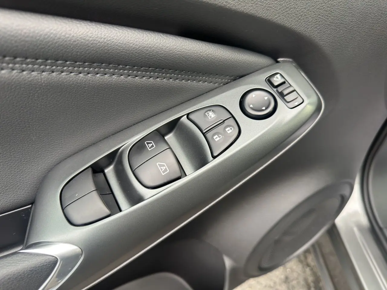 Gros plan sur les commandes de lève-vitres et rétroviseurs côté conducteur du Nissan Juke gris squale 2025.