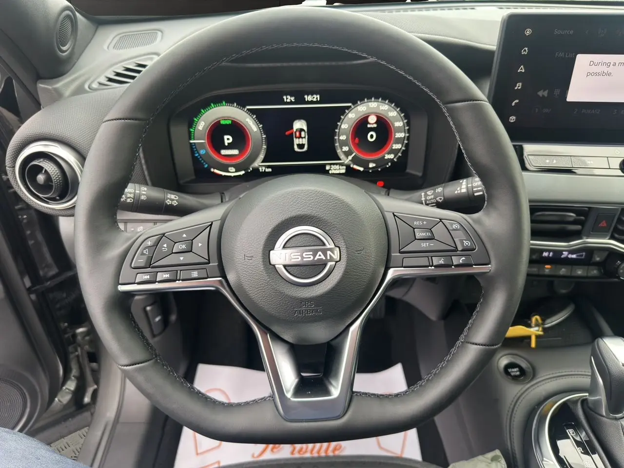 Vue intérieure centrée sur le volant cuir du Nissan Juke 2025 gris squale, avec tableau de bord digital et commandes intégrées.
