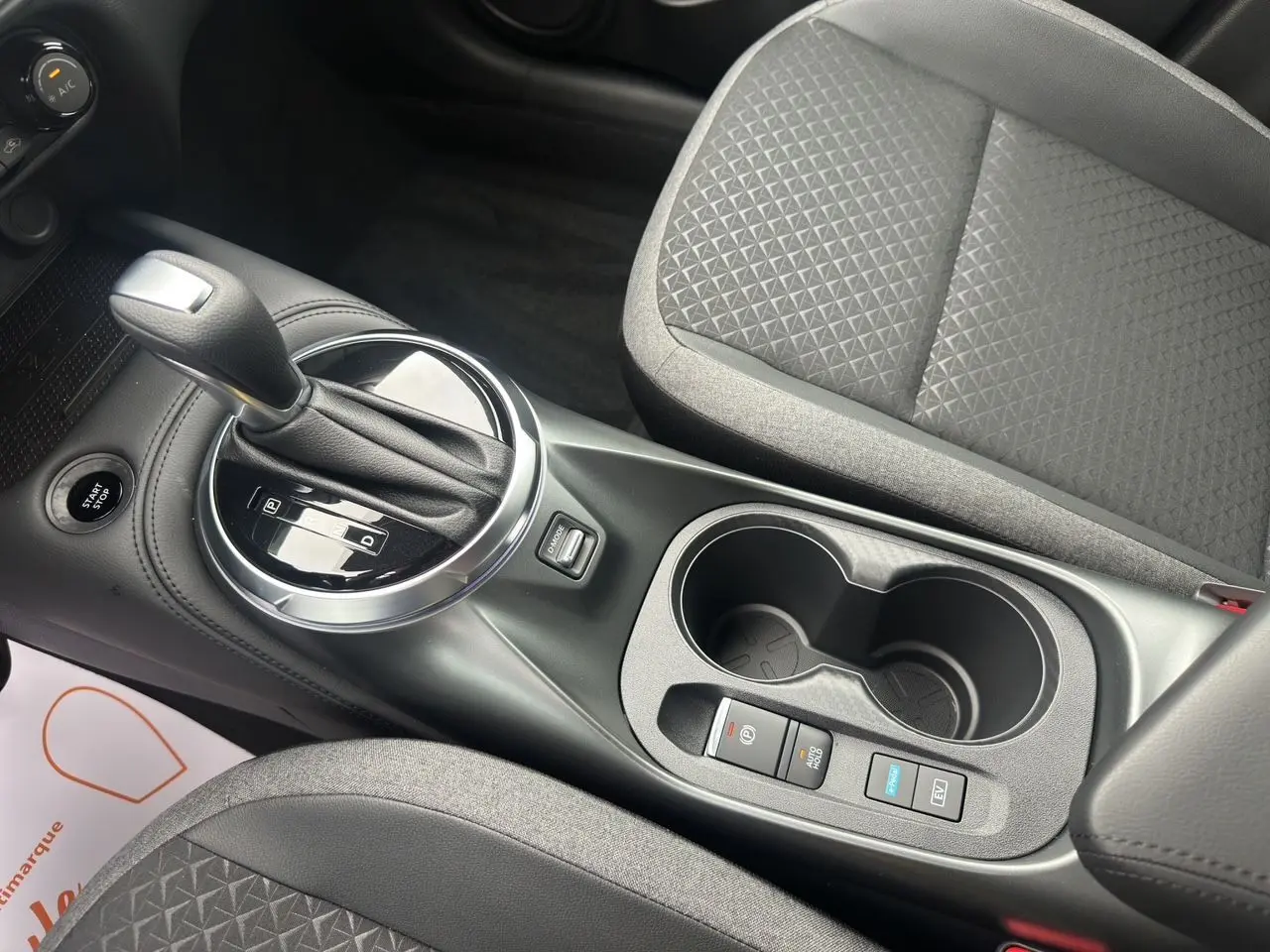Vue rapprochée de la console centrale du Nissan Juke gris squale 2025, avec levier de boîte auto et sièges tissu gris.