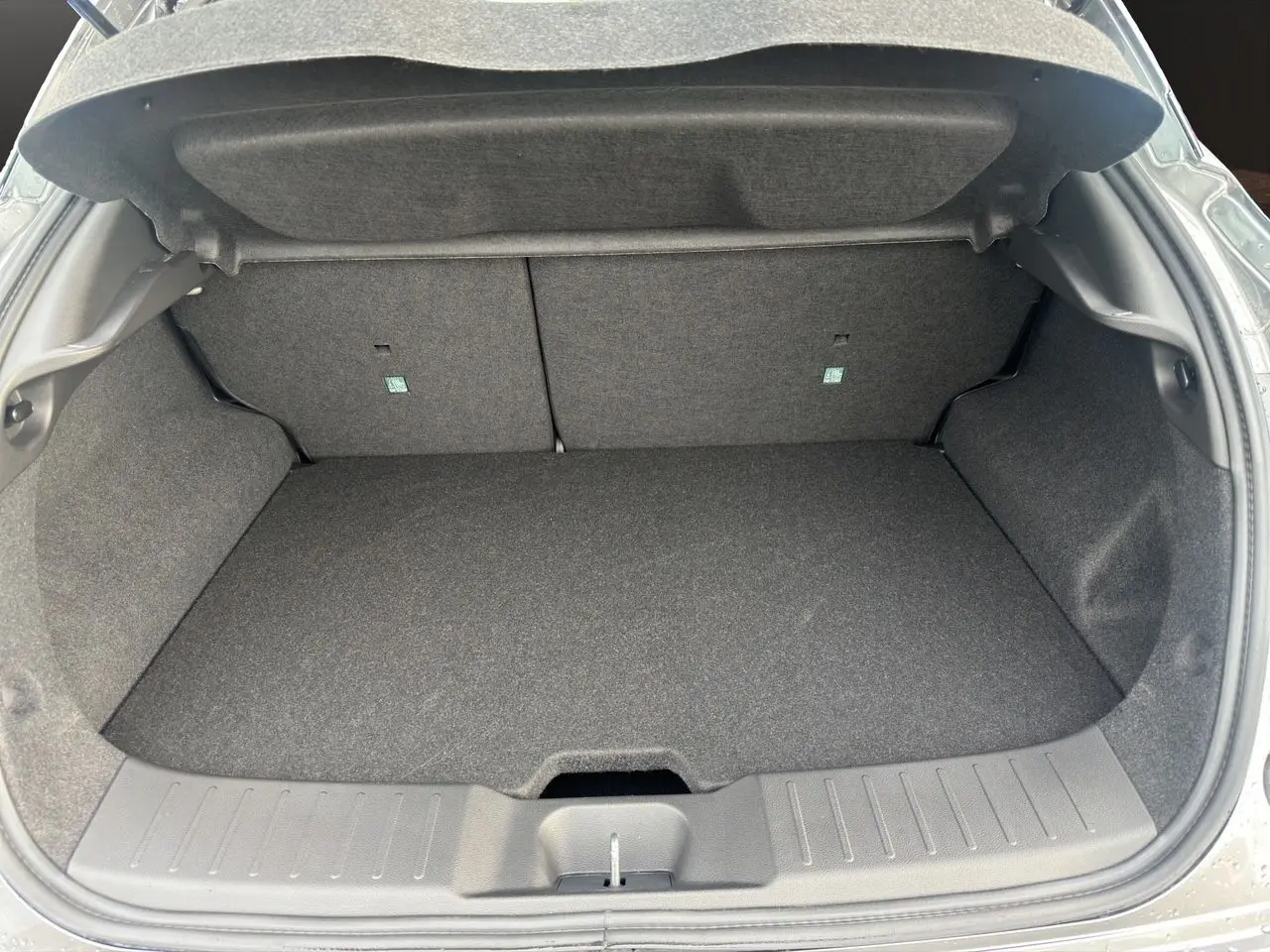Coffre ouvert vu de l’arrière d’un Nissan Juke 1.6 Hybrid 2025 gris squale, espace de chargement vide et propre.