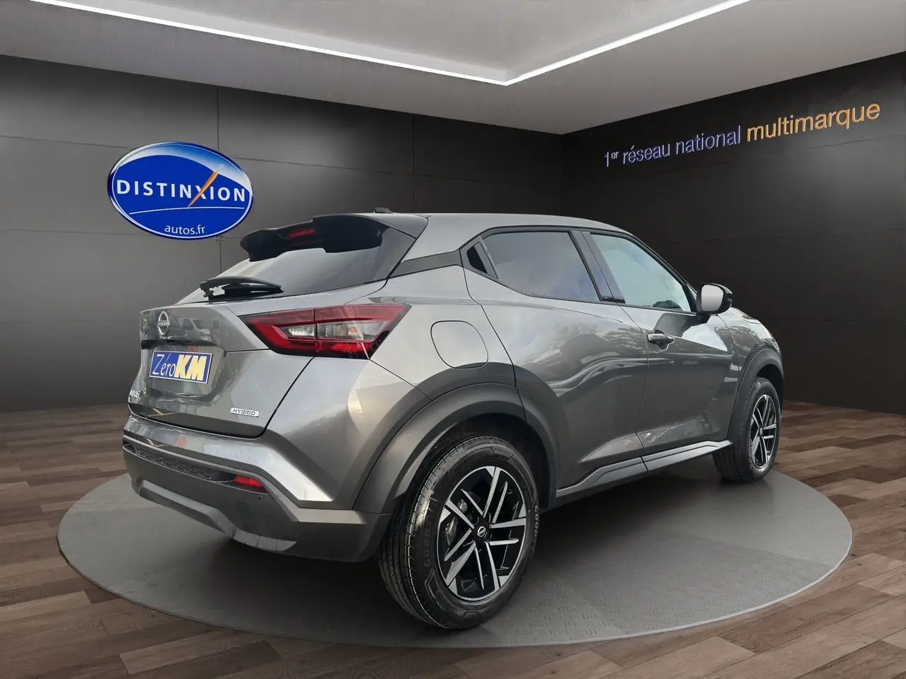 Nissan Juke 2025 gris squale en 3/4 arrière droit, avec jantes noires et détails hybrides visibles sur le hayon.