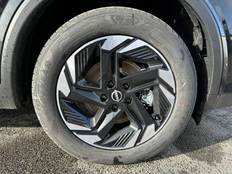 Gros plan sur la roue avant droite du Nissan Qashqai Hybrid e-POWER 2025 en Noir Kuro Métallisé avec jante noire et argentée.