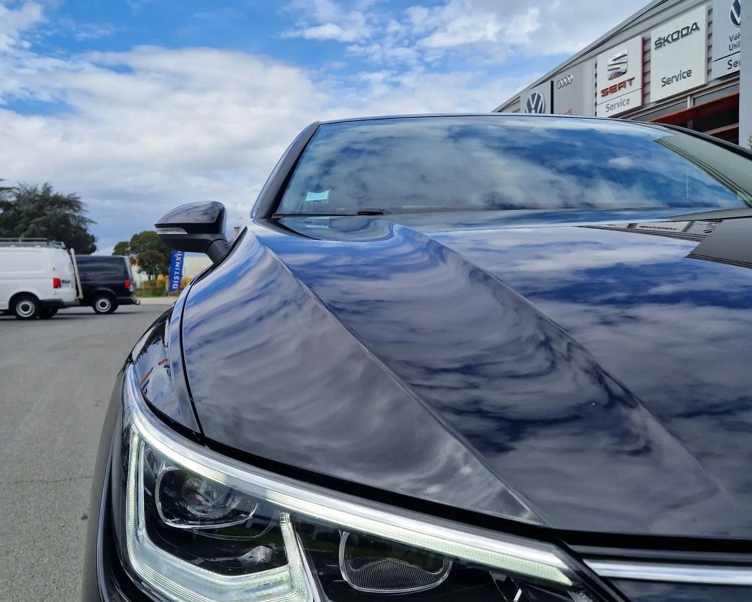 Gros plan sur le phare avant gauche d’une Volkswagen Golf 8 noire intense métal, reflet du ciel sur la carrosserie.