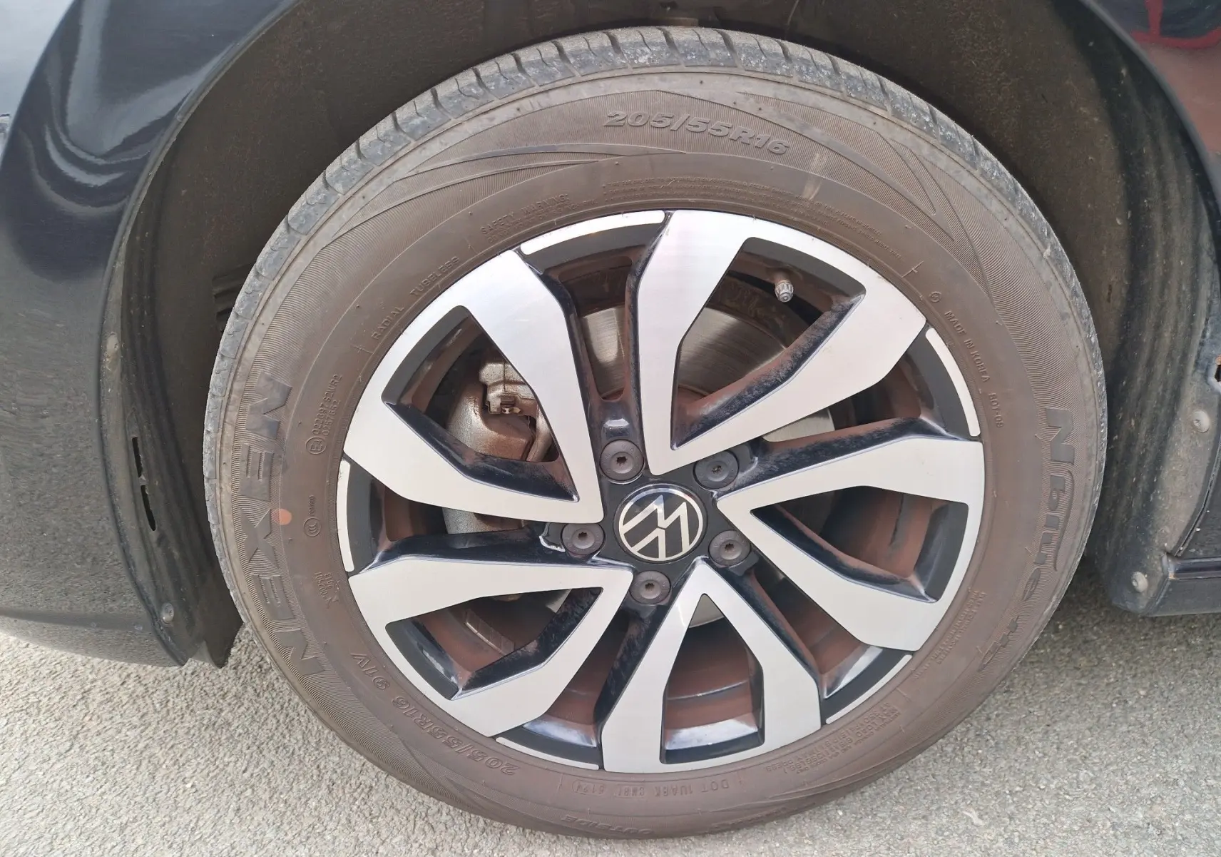 Gros plan sur la roue avant droite d'une Volkswagen Golf 8 noire, jante alliage bicolore avec logo VW central.