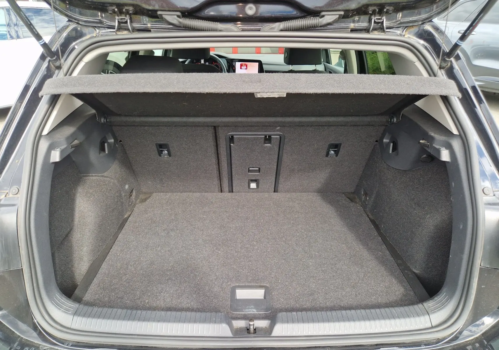 Vue arrière du coffre ouvert d'une Volkswagen Golf 8 noire intense métal, montrant un espace de chargement propre et bien agencé.