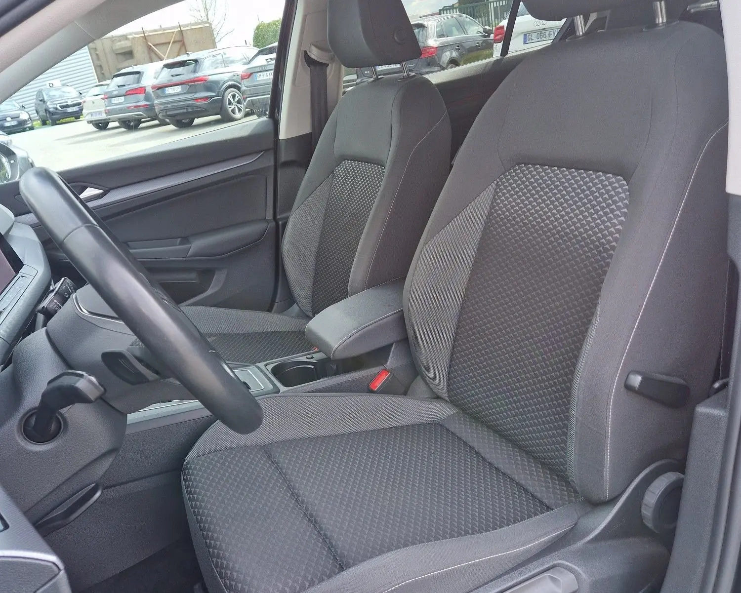 Vue intérieure côté conducteur de la Volkswagen Golf 8 noire, mettant en valeur les sièges tissu gris à motifs et l'habitacle moderne.