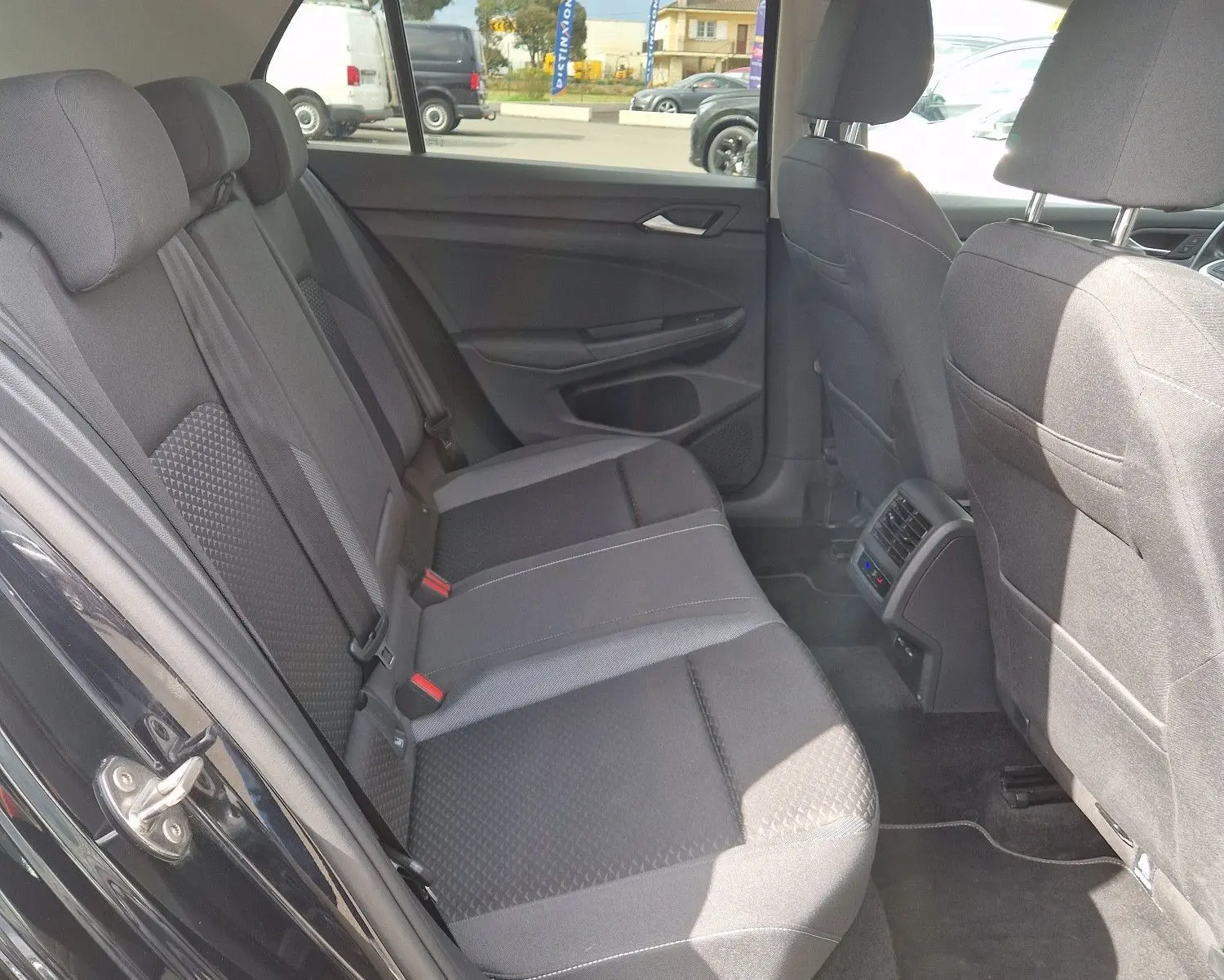 Vue intérieure arrière droite de la Volkswagen Golf 8 noire, montrant les sièges arrière en tissu et les aérations centrales.