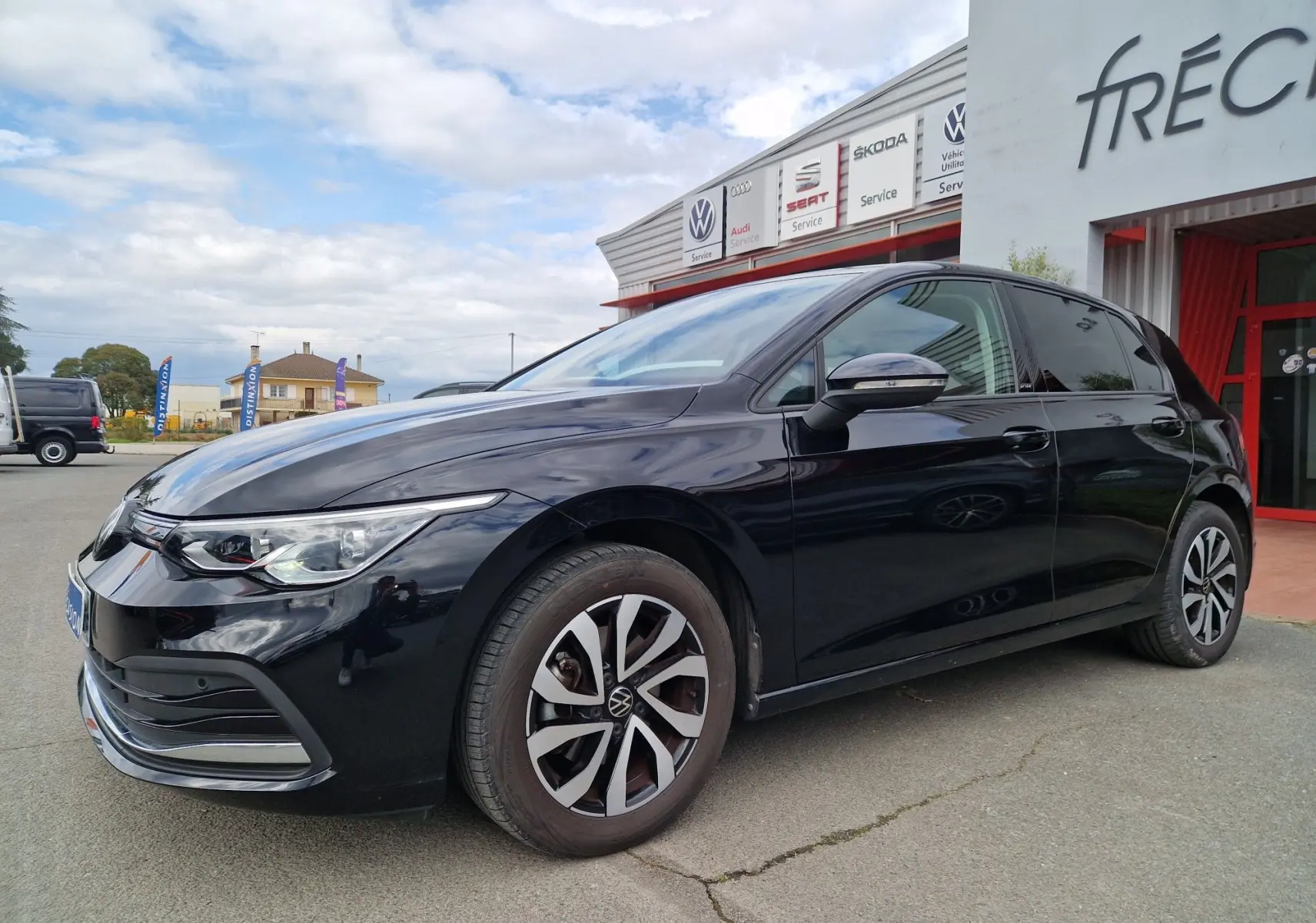 Vue 3/4 avant droit d'une Volkswagen Golf 8 noire intense métal garée devant un garage avec jantes distinctives.