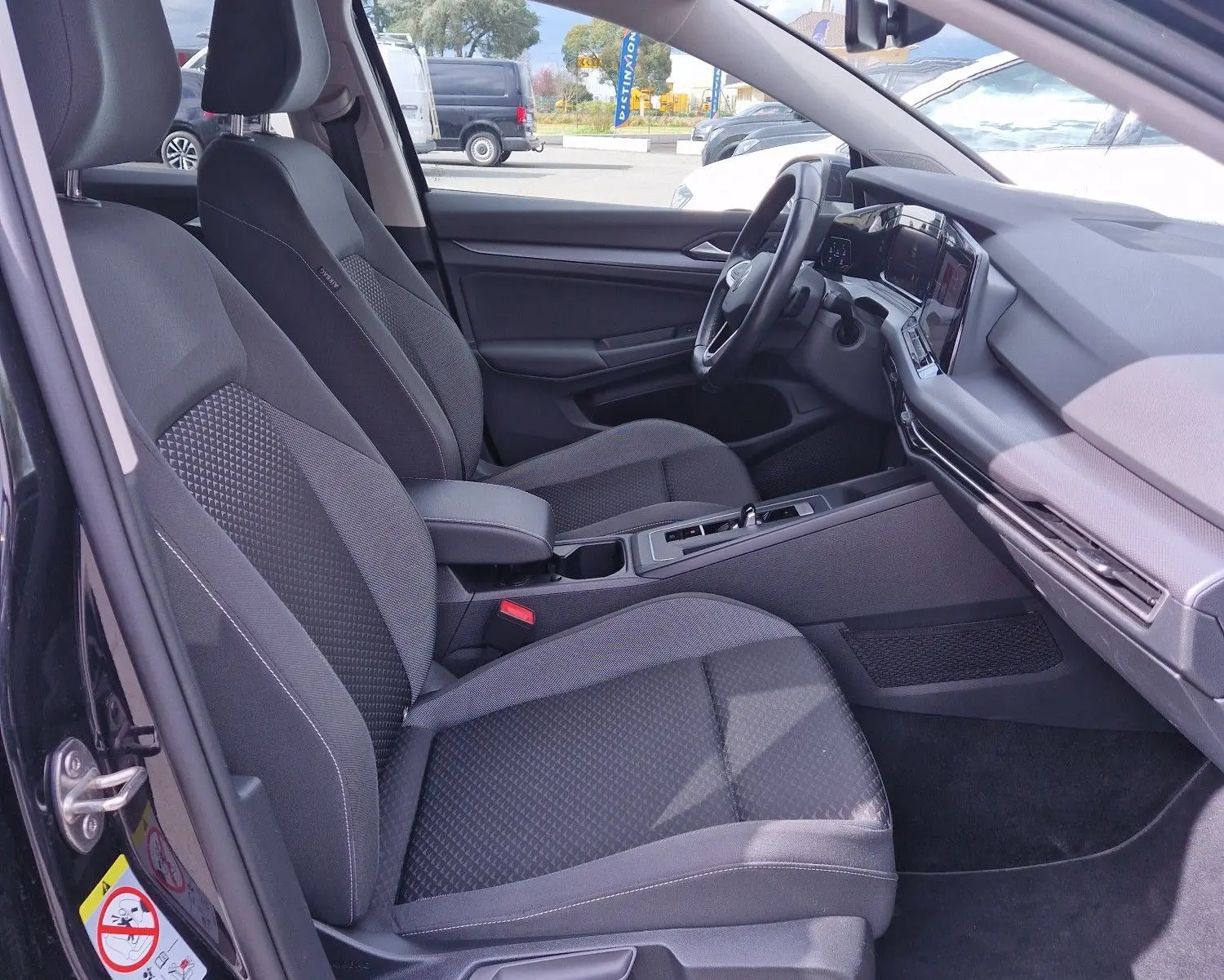 Vue intérieure côté gauche de la Volkswagen Golf 8 noire, montrant les sièges avant et le tableau de bord moderne.