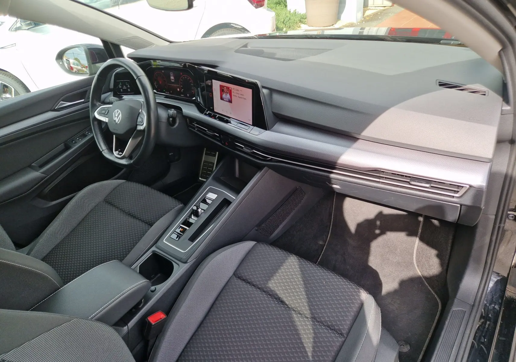 Vue intérieure côté conducteur de la Volkswagen Golf 8 noire, mettant en valeur le tableau de bord numérique et la console centrale moderne.