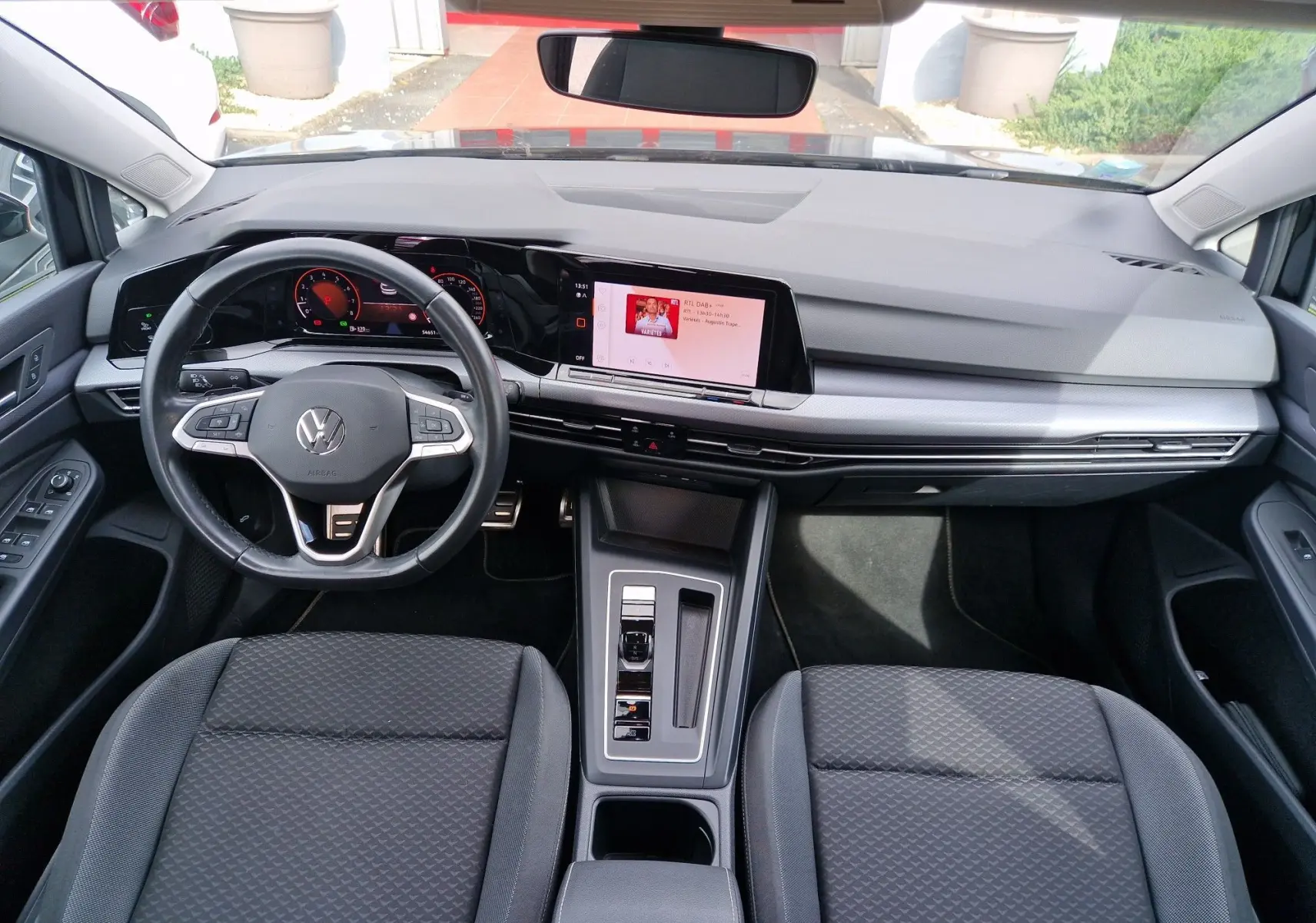 Vue intérieure avant de la Volkswagen Golf 8 noire, mettant en valeur le tableau de bord digital et la console centrale moderne.