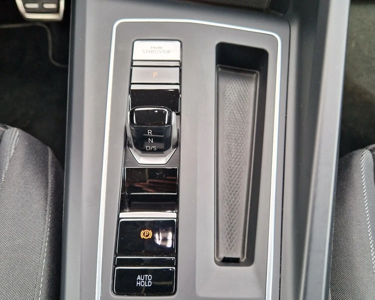 Vue plongeante sur la console centrale noire de la Volkswagen Golf 8, avec levier de vitesses automatique et boutons de contrôle éclairés.