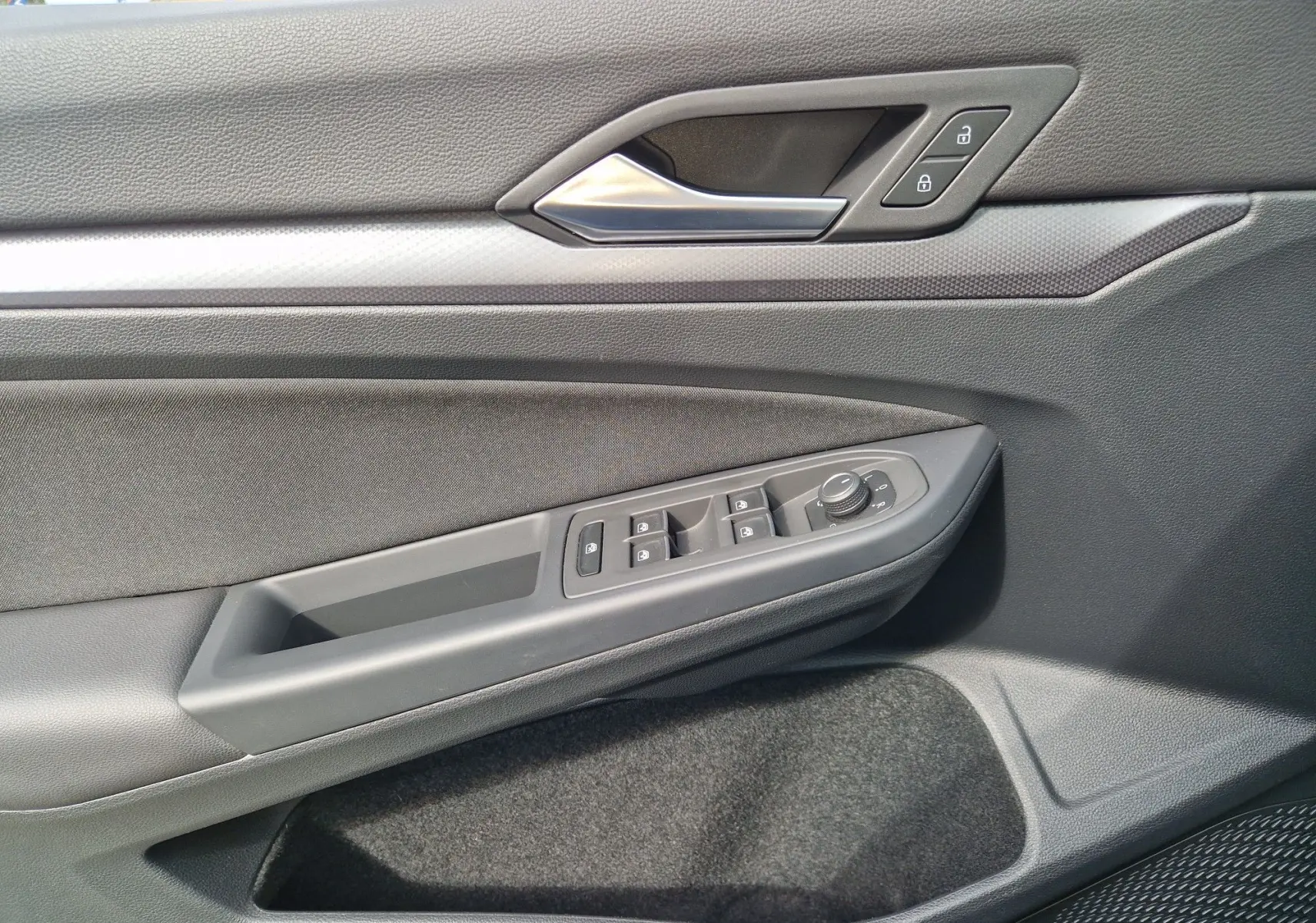 Vue rapprochée de la porte côté gauche de la Volkswagen Golf 8 noire, montrant les commandes des vitres et la poignée intérieure.