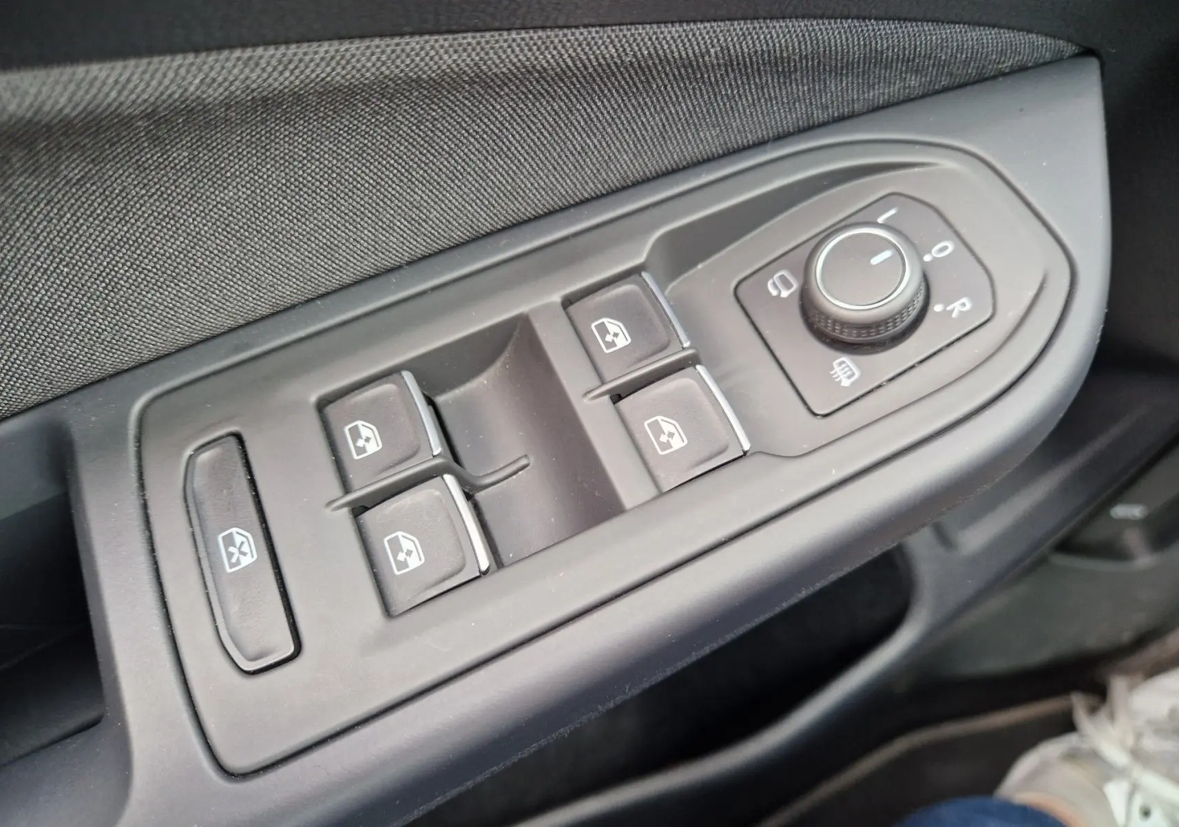 Gros plan sur les commandes des vitres et rétroviseurs côté gauche d’une Volkswagen Golf 8 noire, intérieur tissu gris.