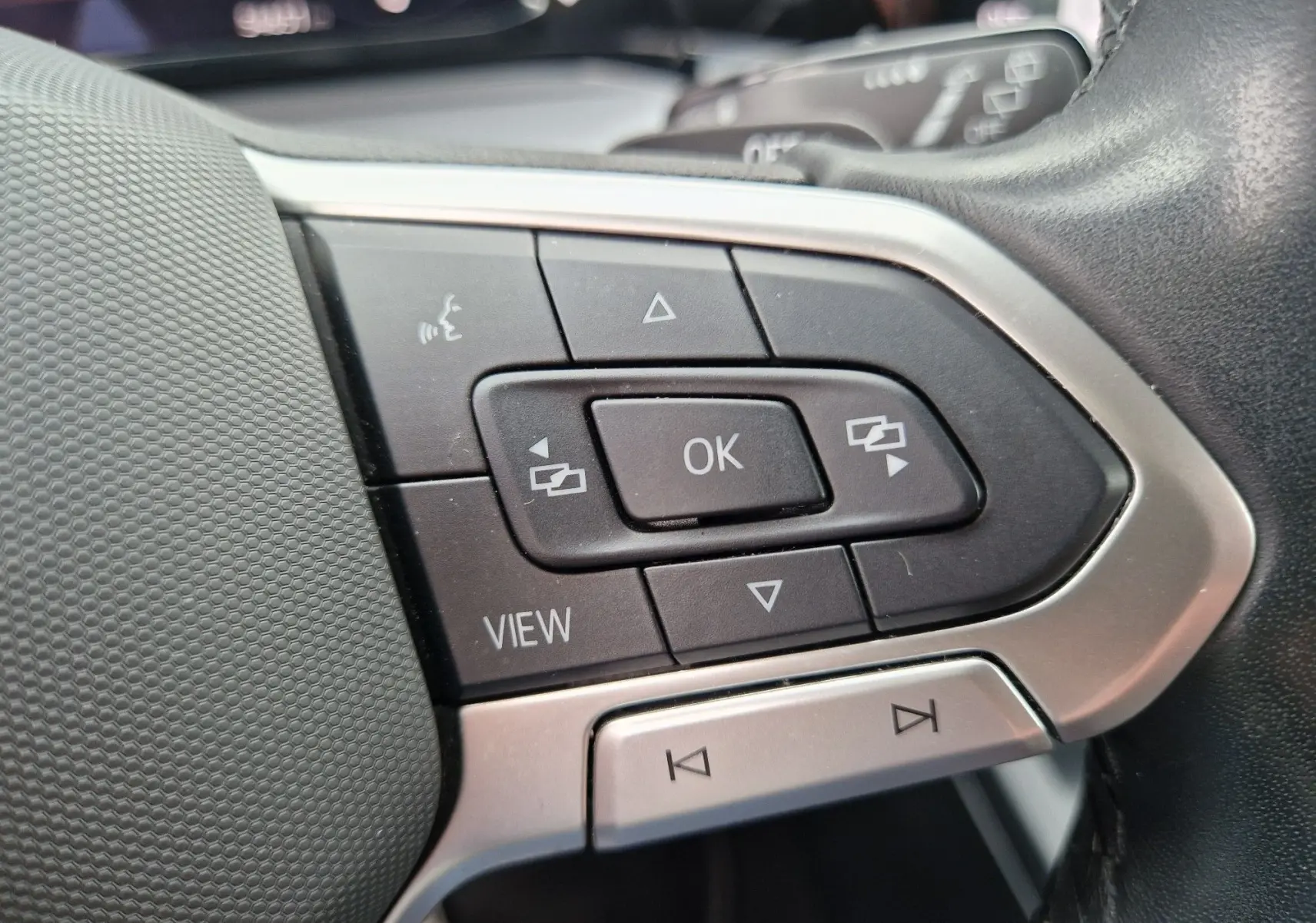 Gros plan sur les commandes multifonctions noires et argent du volant de la Volkswagen Golf 8 noire, côté gauche.