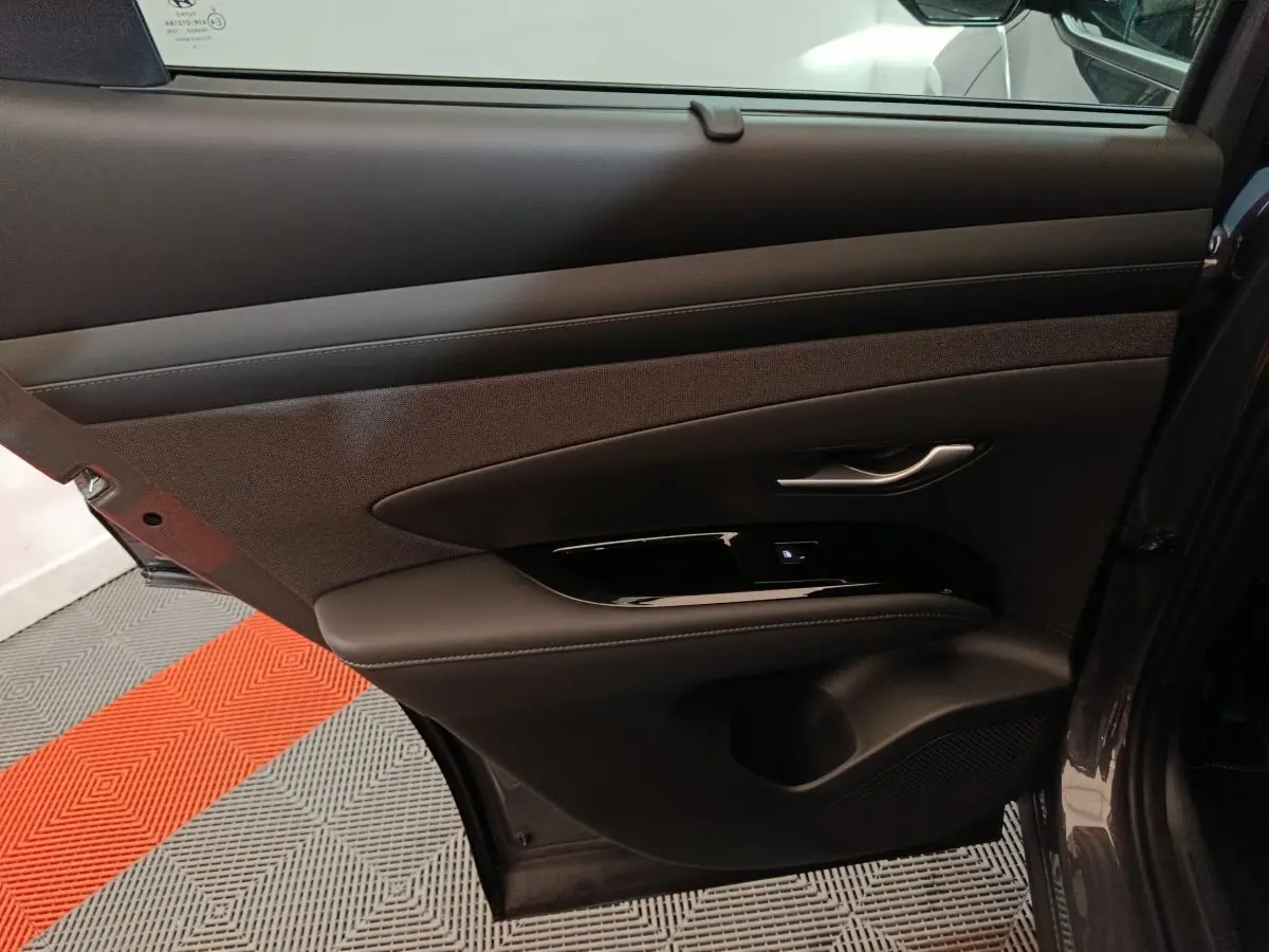 Porte arrière droite ouverte du Hyundai Tucson gris foncé, montrant le panneau intérieur en cuir et tissu avec poignée argentée.