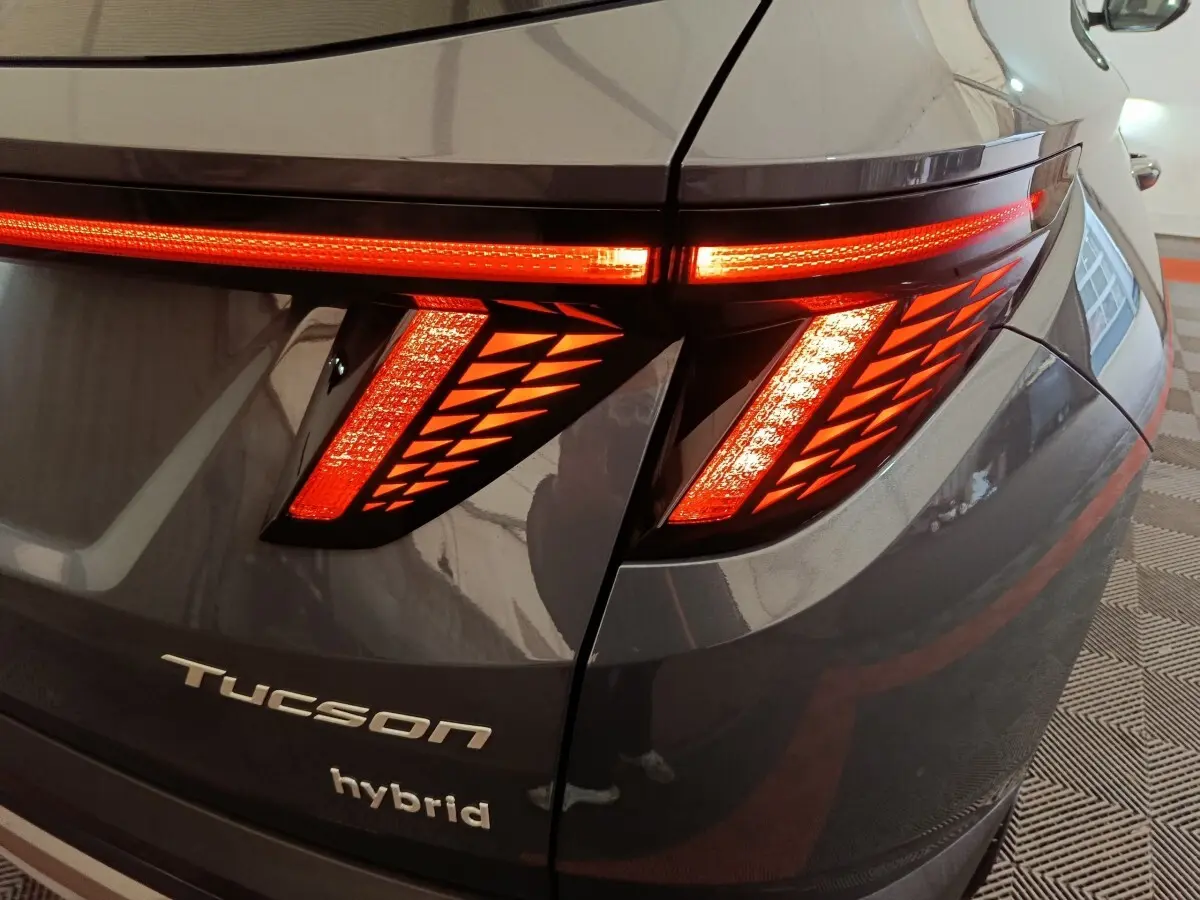 Gros plan sur le feu arrière droit allumé d’un Hyundai Tucson gris foncé hybride avec logo et inscription "hybrid" visibles.