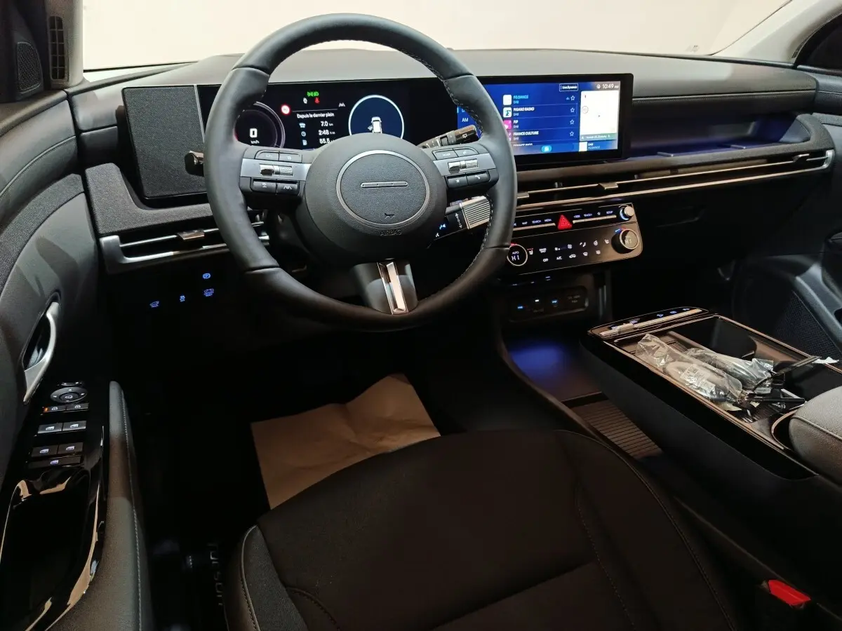 Vue intérieure avant du Hyundai Tucson 1.6 Hybrid 2025, tableau de bord numérique et écran tactile central lumineux.