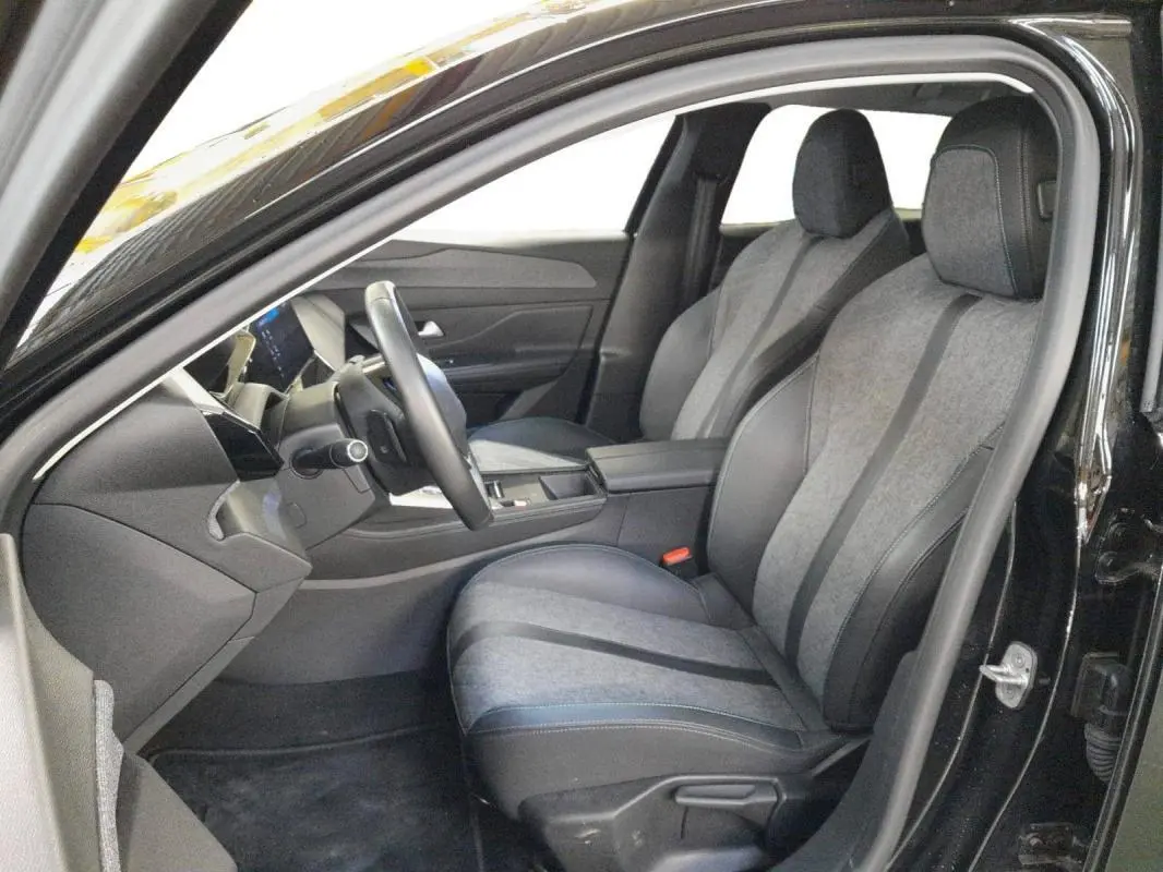 Intérieur avant droit de la Peugeot 408 PHEV 180 Allure 2024 noir, sièges tissu et cuir, volant et console visibles.