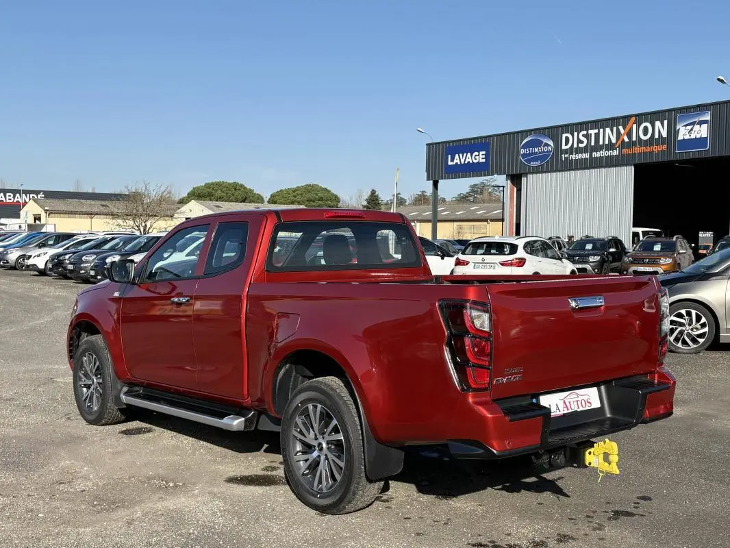 Vue 3/4 arrière droite d'un Isuzu D-MAX rouge métallisé avec jantes aluminium et attelage visible en concession.