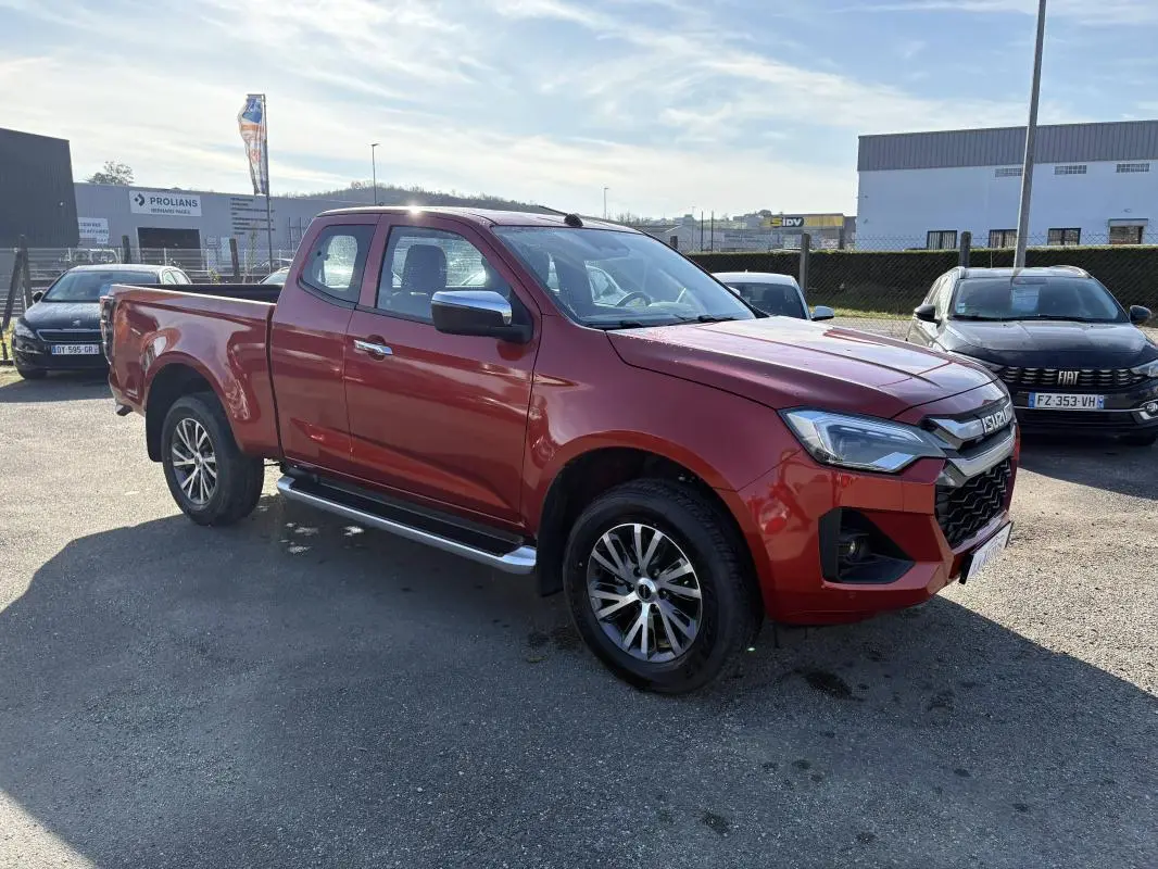 Isuzu D-MAX orange vue 3/4 avant droit, avec jantes aluminium et marchepieds latéraux visibles.