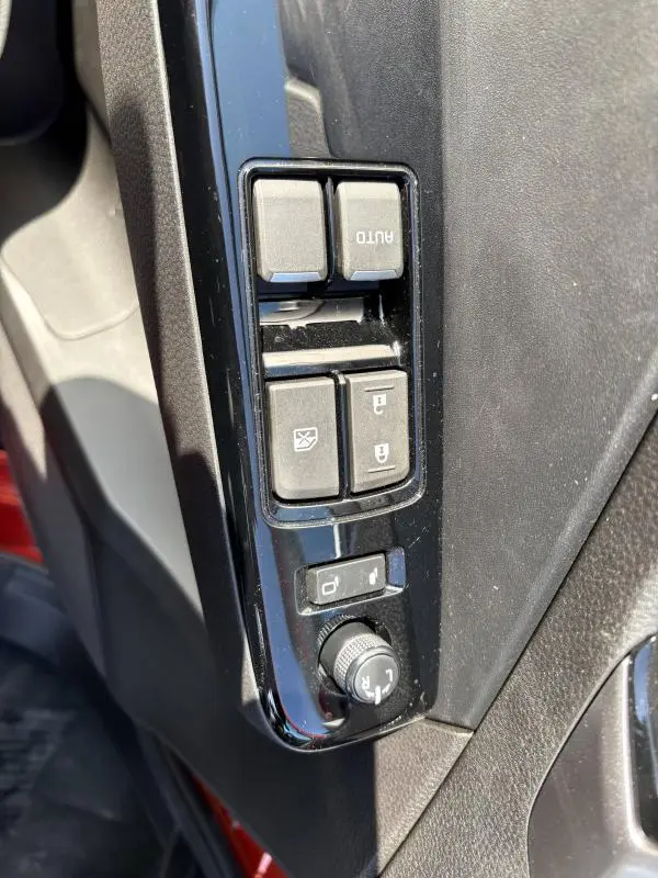 Gros plan sur les commandes des vitres et des rétroviseurs côté conducteur d'un Isuzu D-MAX orange 2026.