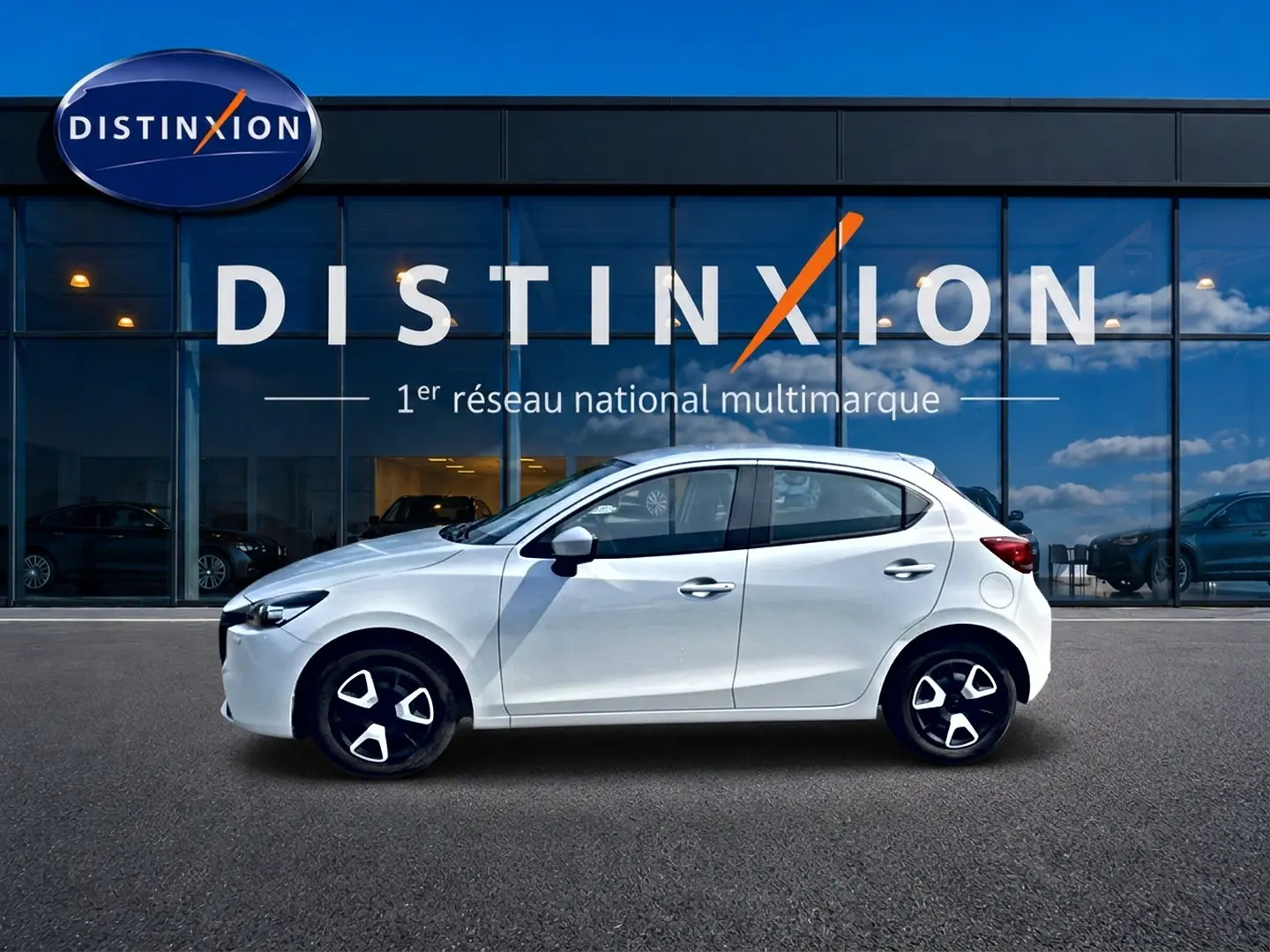 Vue de profil côté gauche d'une Mazda2 blanche 2024 avec jantes noires et détails modernes devant une vitrine Distinxion.