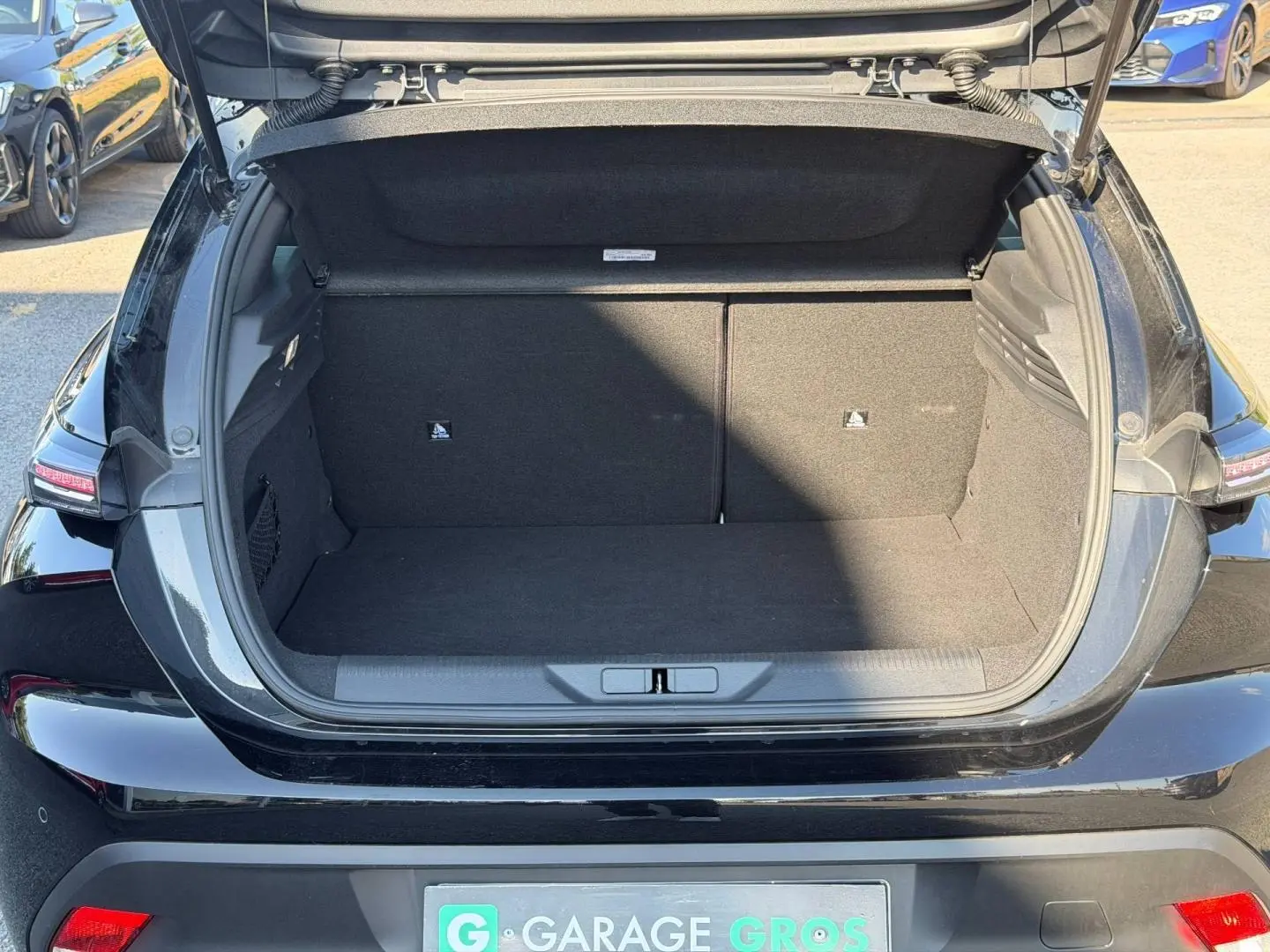 Coffre ouvert vu de l'arrière d'une Peugeot 308 e-308 noire Perla Nera avec feux arrière LED visibles.