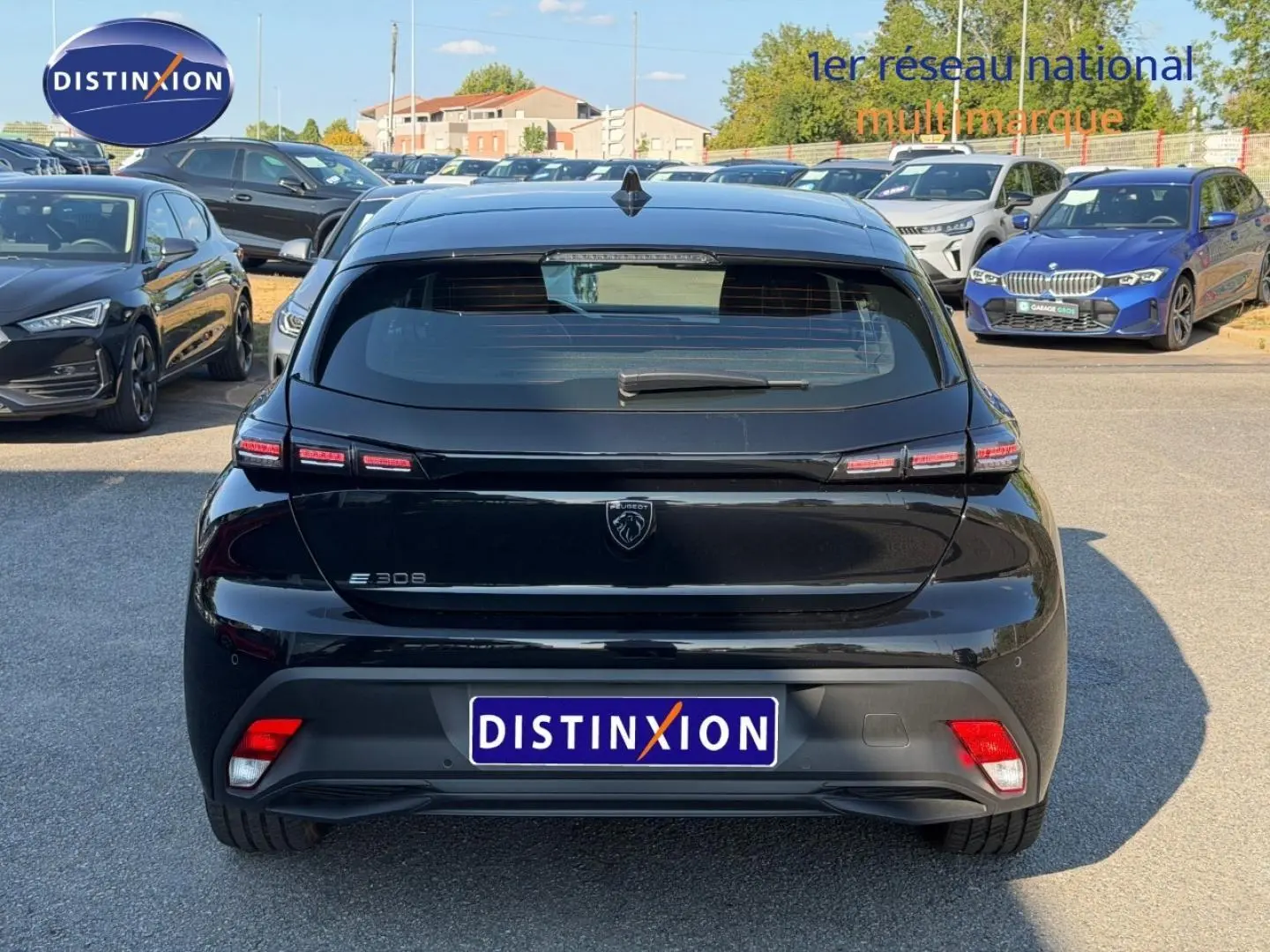 Vue arrière d'une Peugeot e-308 noire Perla Nera avec feux LED distinctifs et logo lion central sur parking.