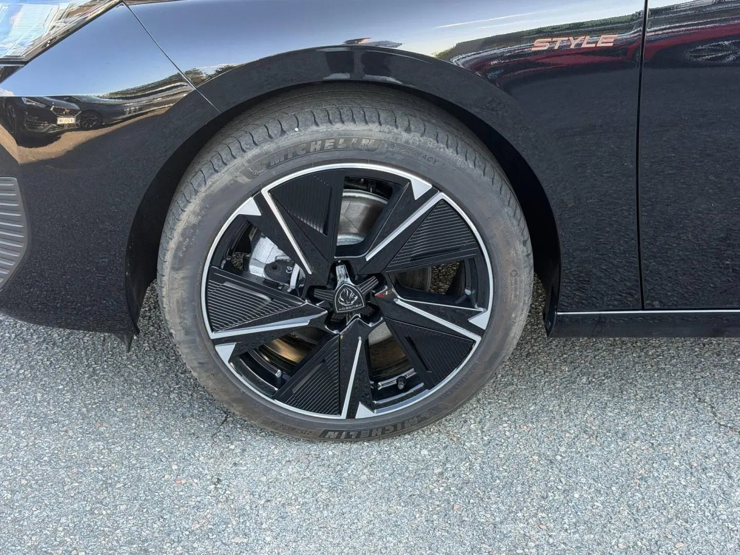 Gros plan sur la roue avant gauche noire et jante alu au design géométrique de la Peugeot e-308 Style noir Perla Nera.