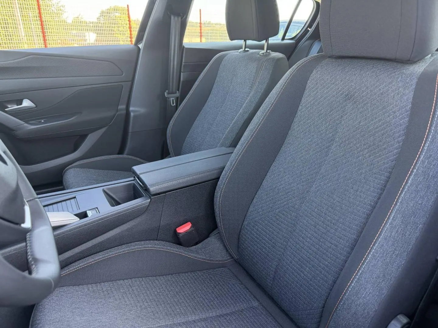 Vue intérieure rapprochée des sièges avant en tissu gris avec surpiqûres orange de la Peugeot e-308 2025.