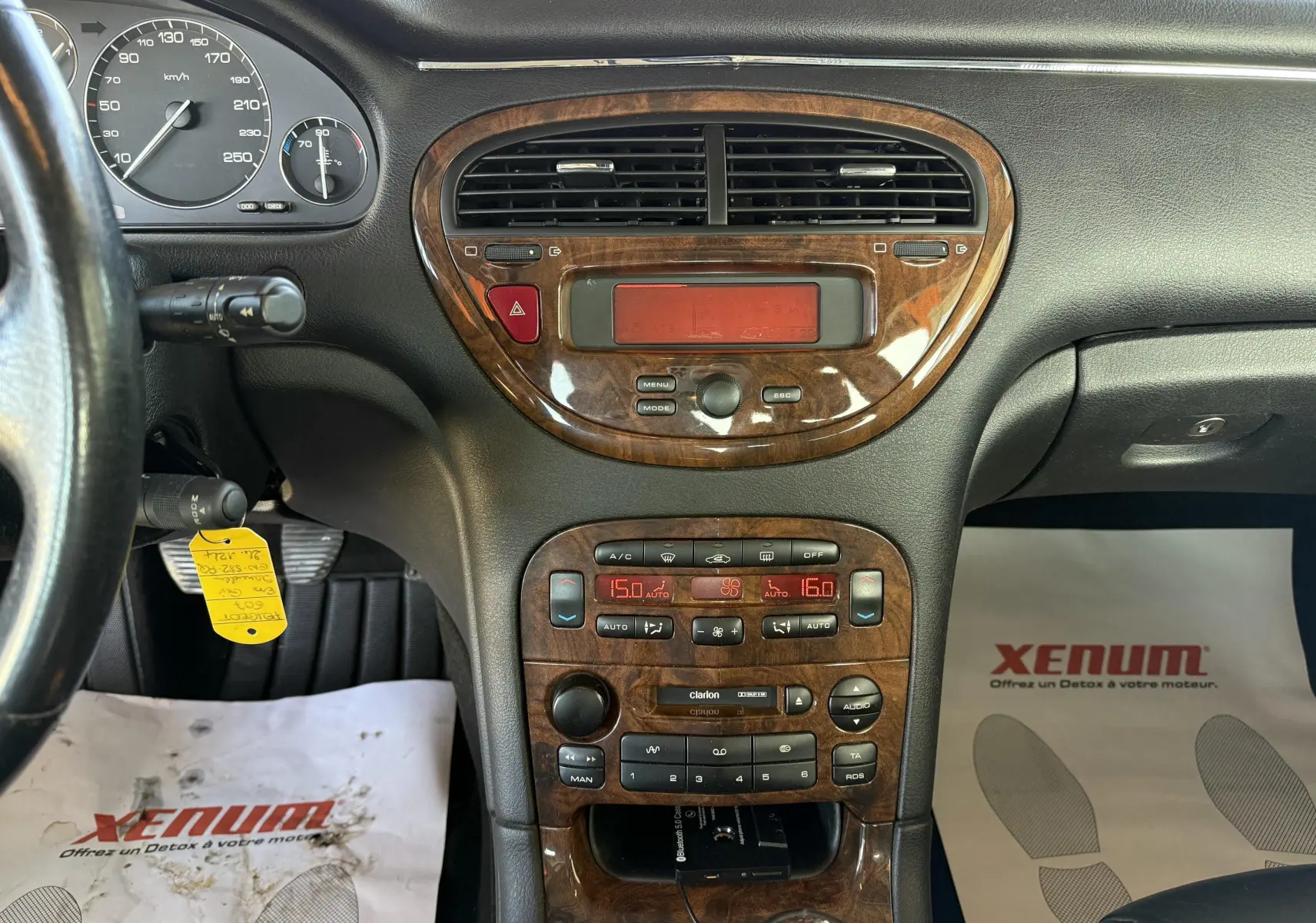 Tableau de bord en bois et noir de la Peugeot 607 gris, vue frontale centrée sur la console centrale et les commandes climatiques.