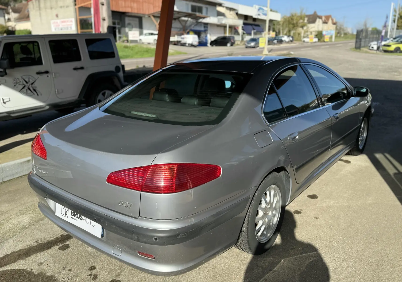 Peugeot 607 gris vue 3/4 arrière droit, avec feux arrière rouges et jantes alliage argentées.