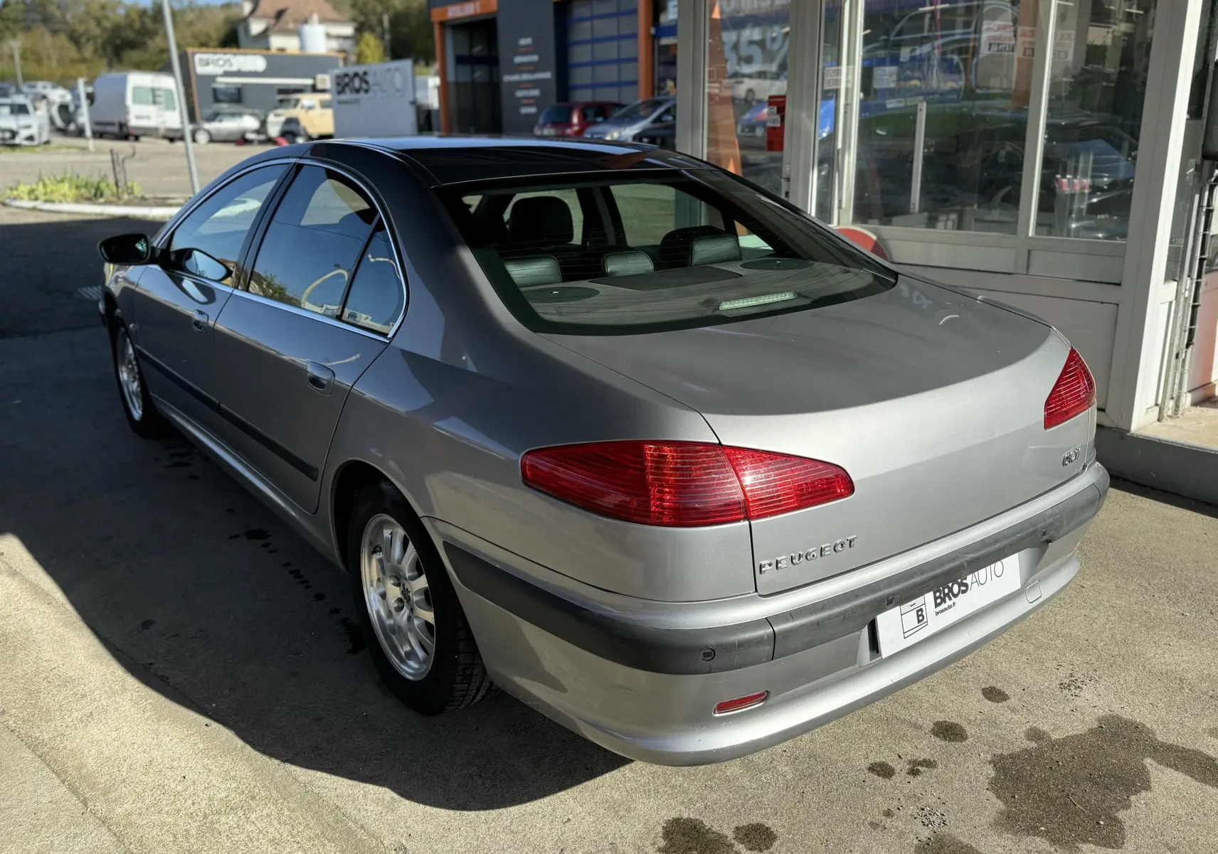 Peugeot 607 gris vue 3/4 arrière côté gauche, avec feux rouges et jantes alliage en extérieur.