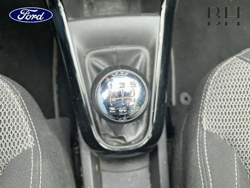 Le levier de vitesses manuel vu de dessus dans l'habitacle, entouré de sièges en tissu gris à motifs.