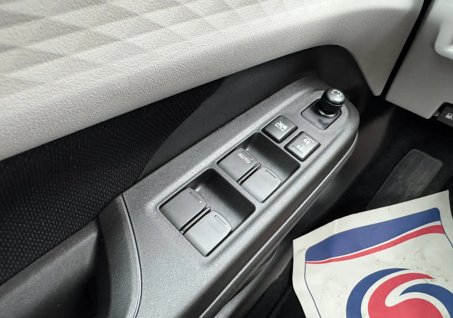 Gros plan sur la commande des vitres électriques côté conducteur de la Suzuki Swift 1.2 Privilège Hybrid blanche, intérieur noir.