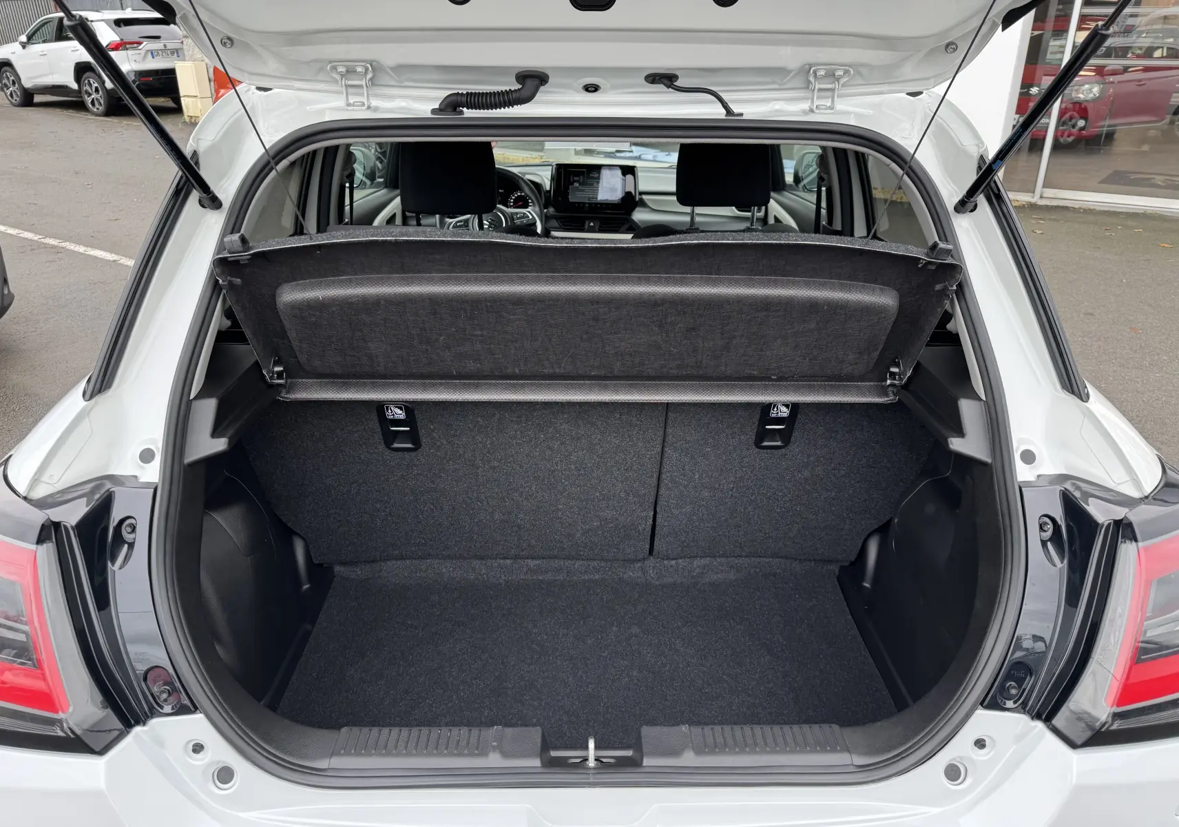 Coffre ouvert vu de l'arrière d'une Suzuki Swift 1.2 Privilège Hybrid blanche, avec cache-bagages relevé.