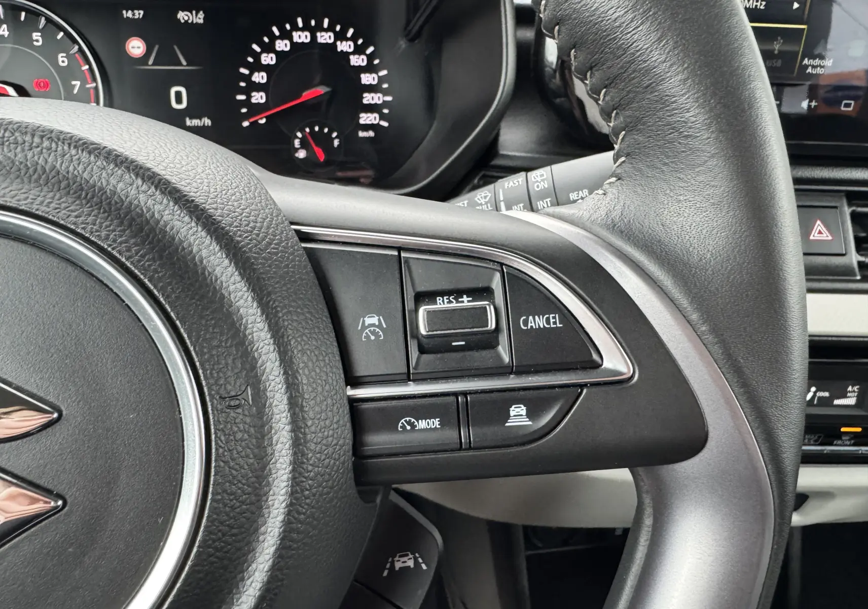 Gros plan sur les commandes de régulateur de vitesse au volant cuir noir de la Suzuki Swift 1.2 Privilège Hybrid blanche.