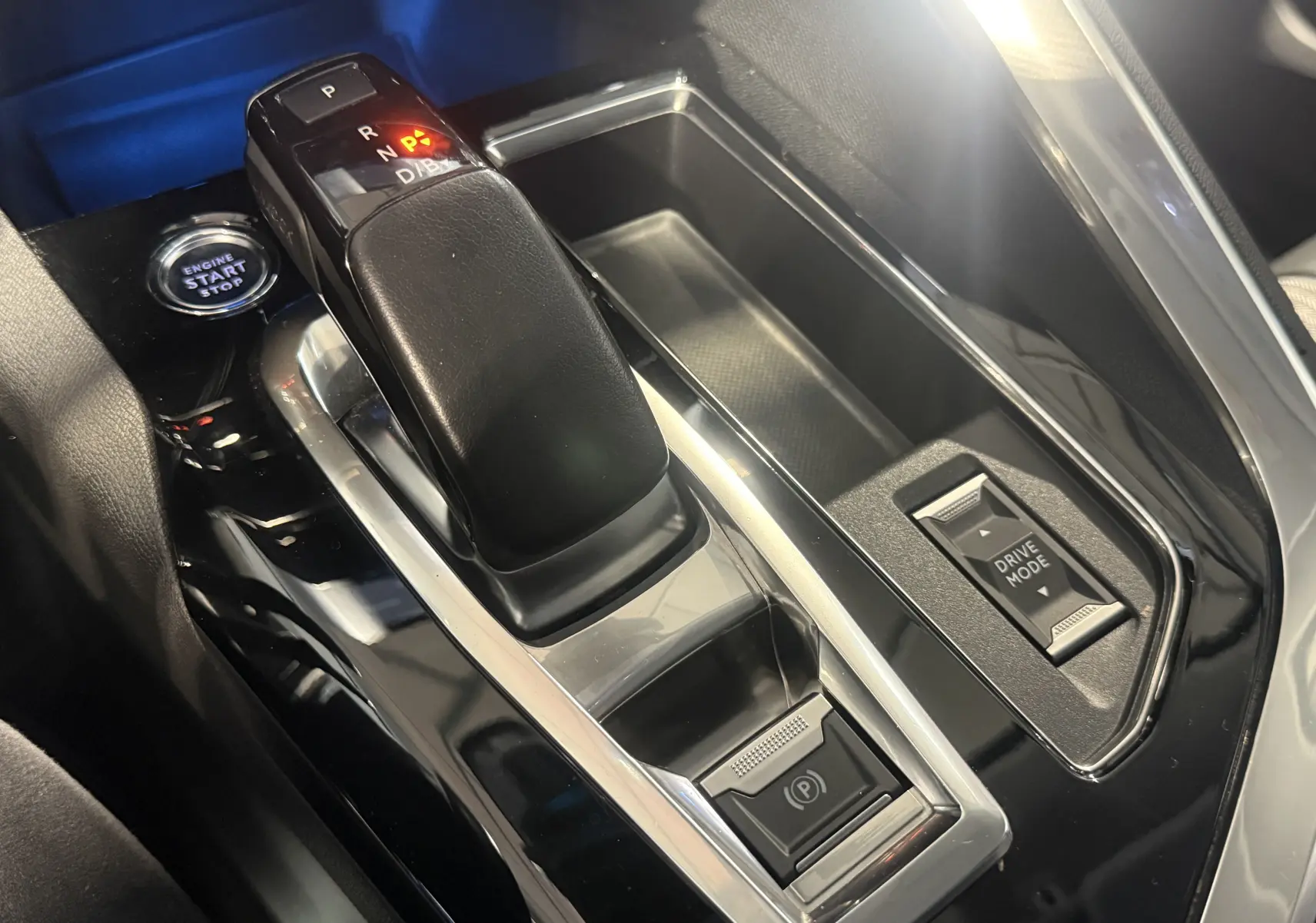 Gros plan sur la console centrale noire du Peugeot 3008 Hybrid 2025 avec levier de vitesse automatique et bouton Drive Mode.