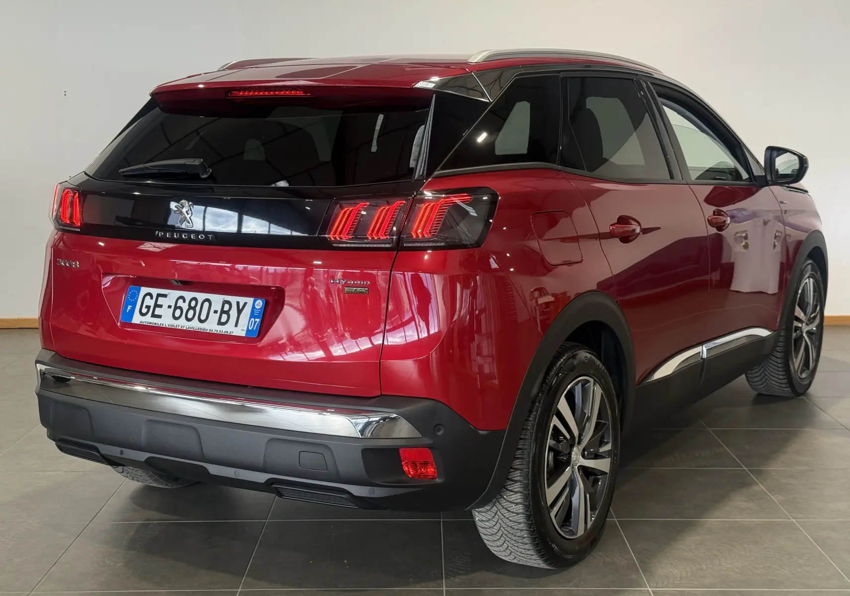 Vue 3/4 arrière droite du Peugeot 3008 Hybrid rouge 2025 avec feux arrière à griffes et toit noir brillant.