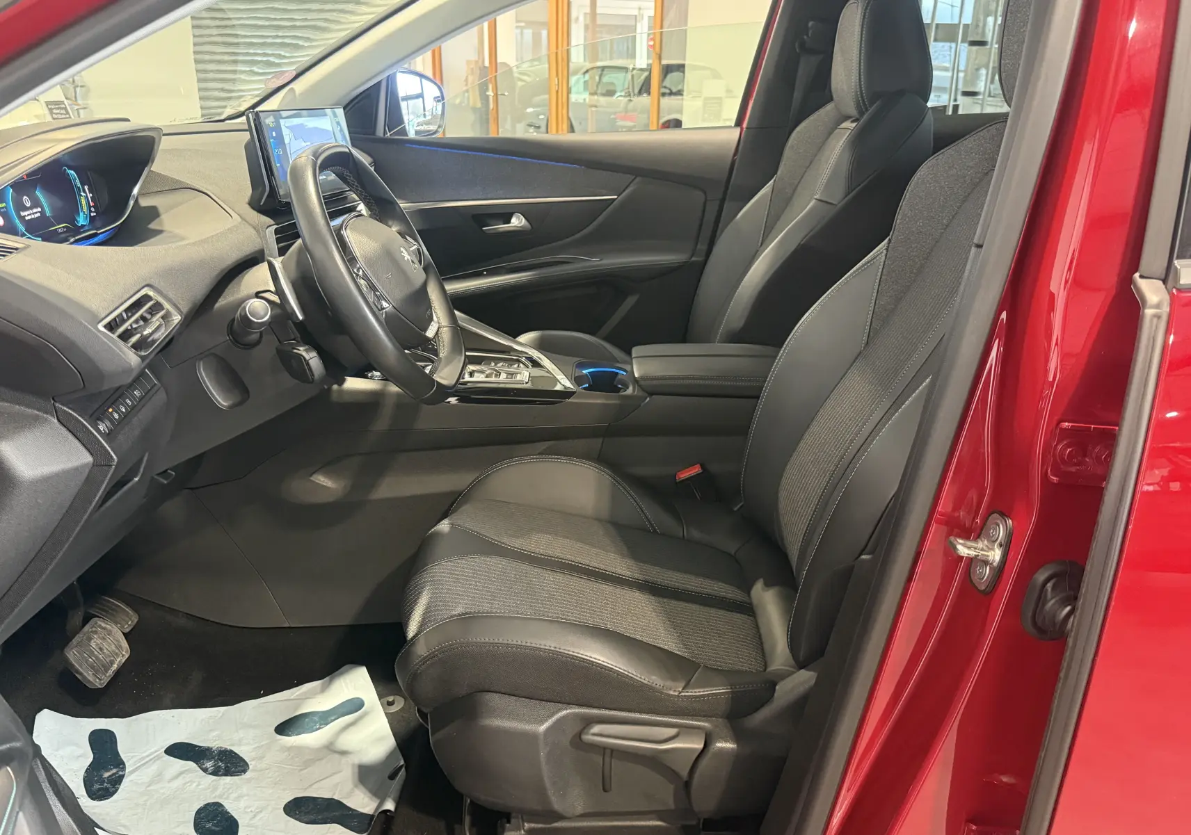 Intérieur côté conducteur du Peugeot 3008 Hybrid rouge 2025, vue en léger angle avec sièges noirs et tableau de bord numérique.