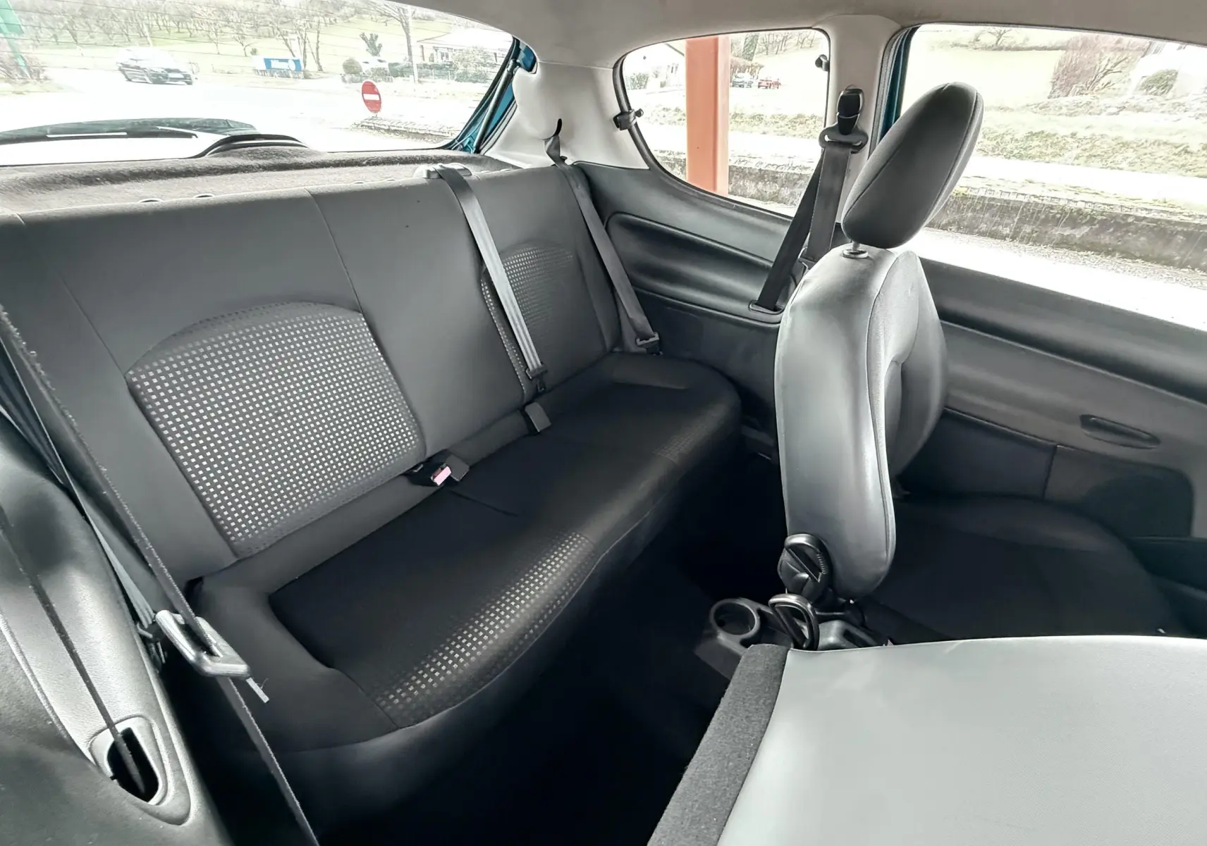 Vue intérieure arrière droite de la Peugeot 206+ bleue, montrant la banquette arrière en tissu noir et la portière ouverte.