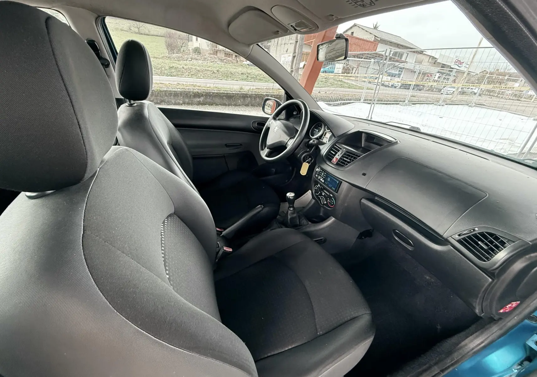 Vue intérieure arrière côté droit de la Peugeot 206+ 1.1 i 60 avec sièges tissu noir et ceintures de sécurité visibles.