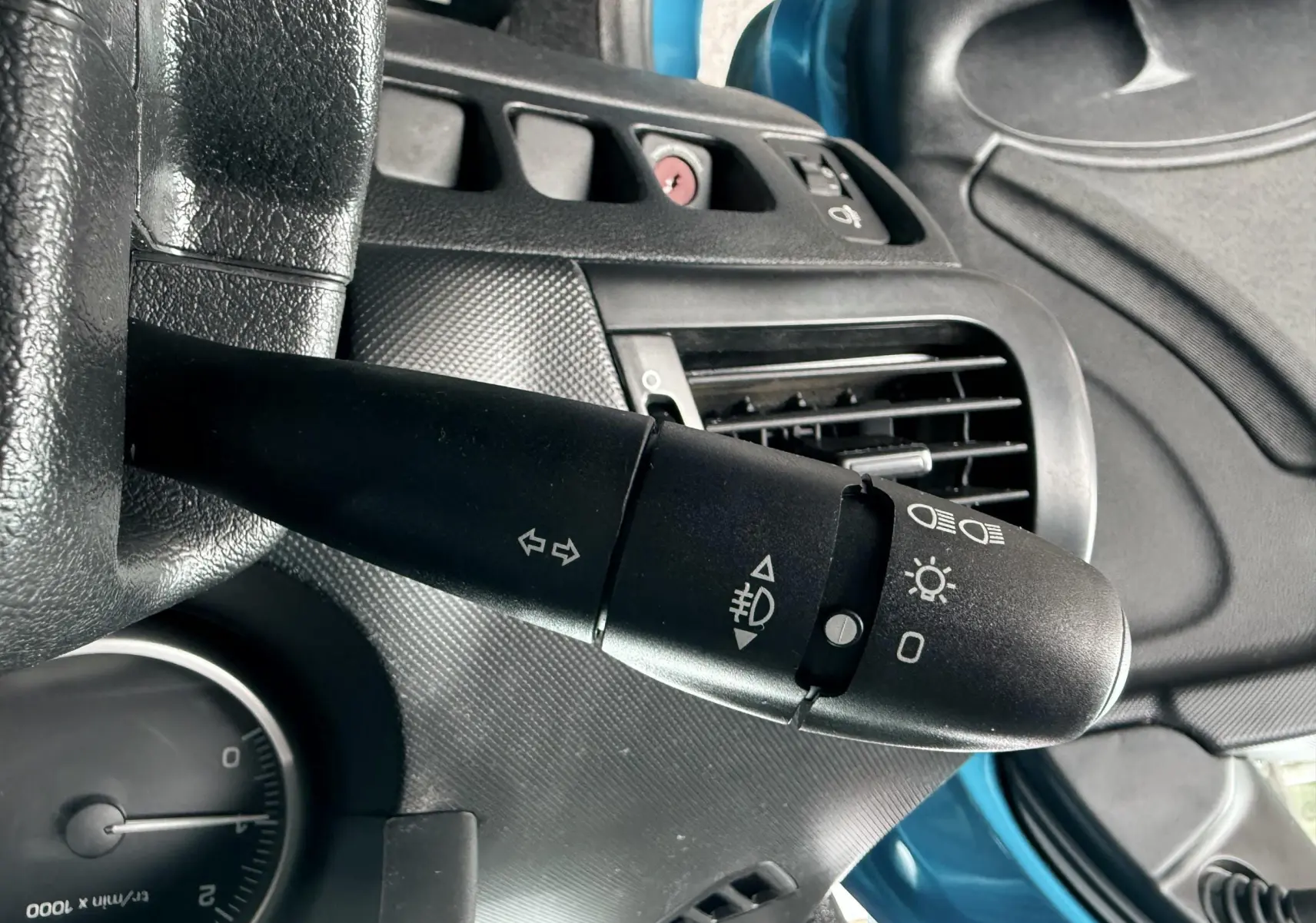 Vue intérieure centrée sur le volant noir de la Peugeot 206+ bleu, avec tableau de bord et console centrale visibles.