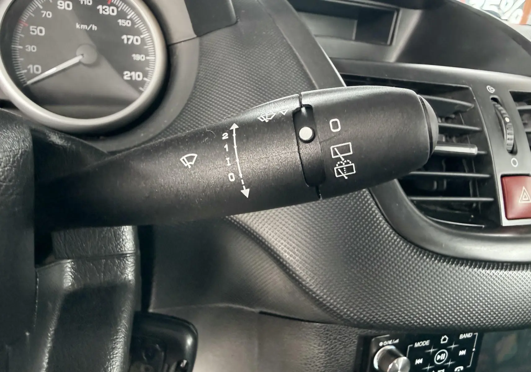 Gros plan sur la commande de clignotants à gauche du volant d'une Peugeot 206+ bleu, intérieur noir.