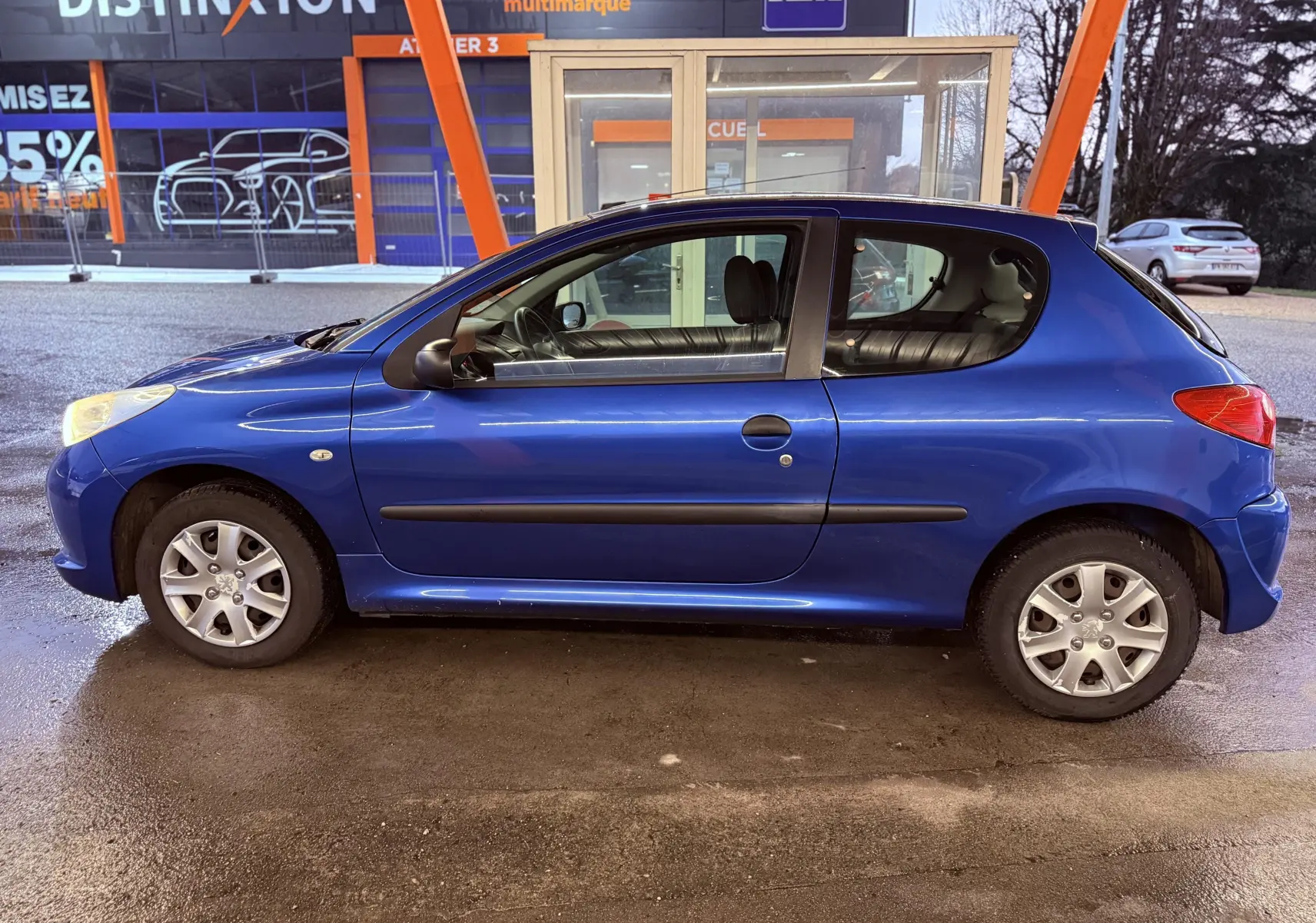 Vue avant d’une Peugeot 206+ bleue de 2011 avec phares allumés et plaque Distinxion visible.