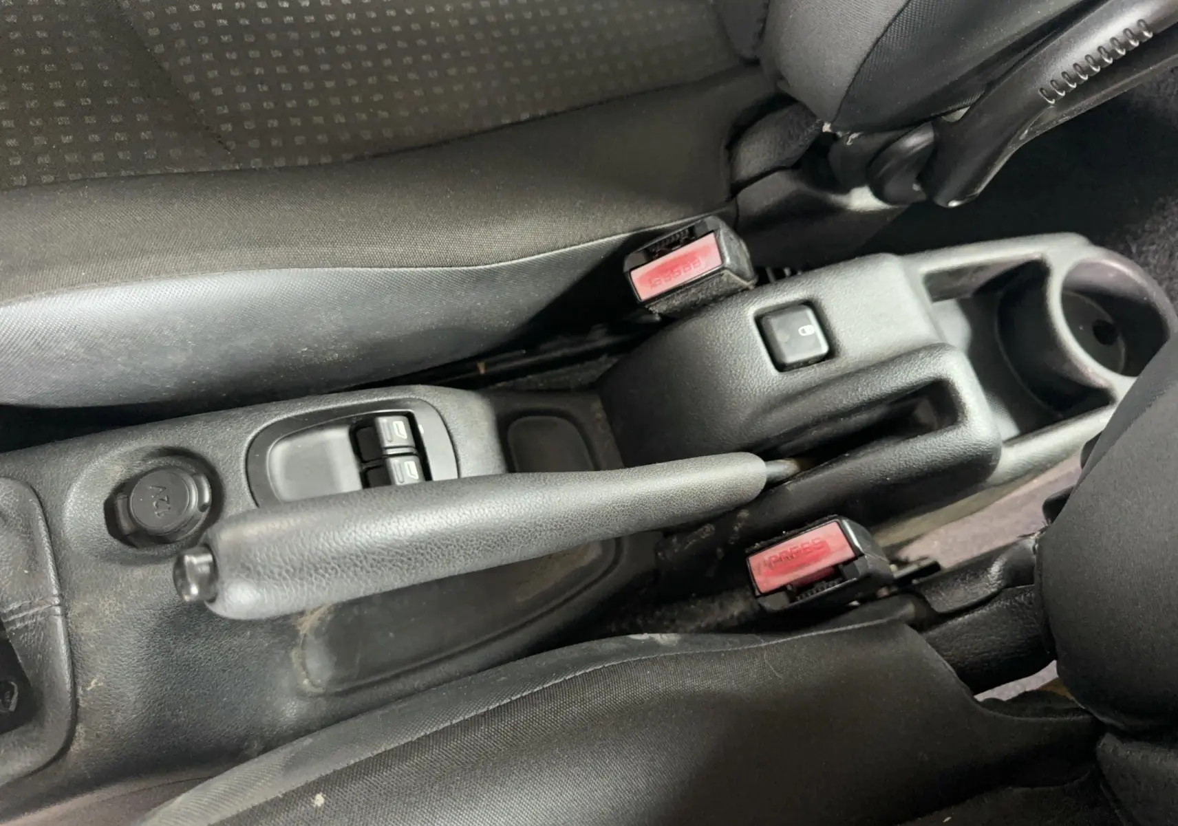 Gros plan sur la console centrale noire de la Peugeot 206+ 2011, montrant les commandes de vitres électriques et prise 12V.